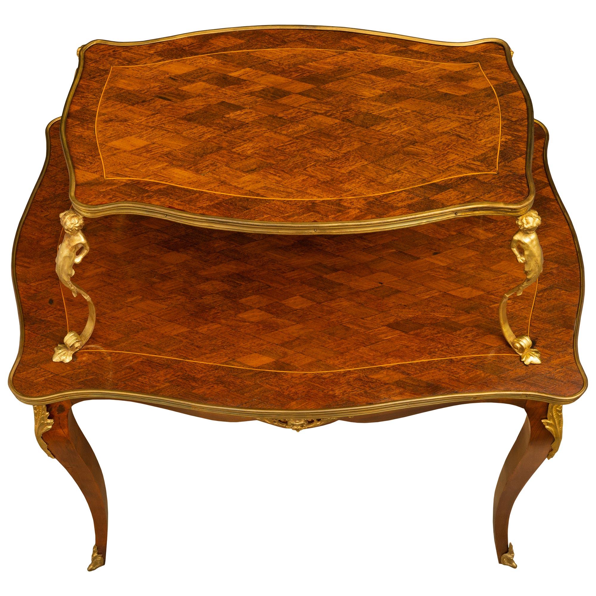 A French 19th century Louis XV style two-tier mahogany and ormolu serving table. The table is raised on cabriole legs with ormolu sabots and top ormolu mounts. A parquetry lattice design decorated the top of each surface with four ormolu cherubs