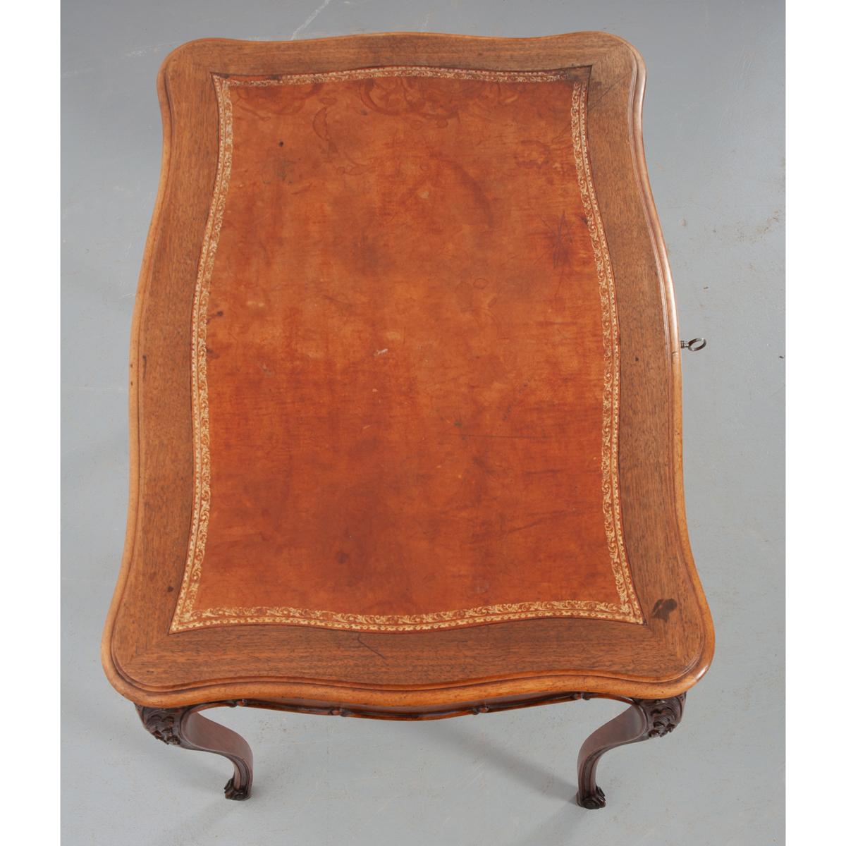 A fantastic mahogany desk that could serve as an occasional table or a small writing desk. This beautiful antique features exceptional decorative carvings, all done by hand, that are found on antiques influenced by Louis XV. The writing surface has