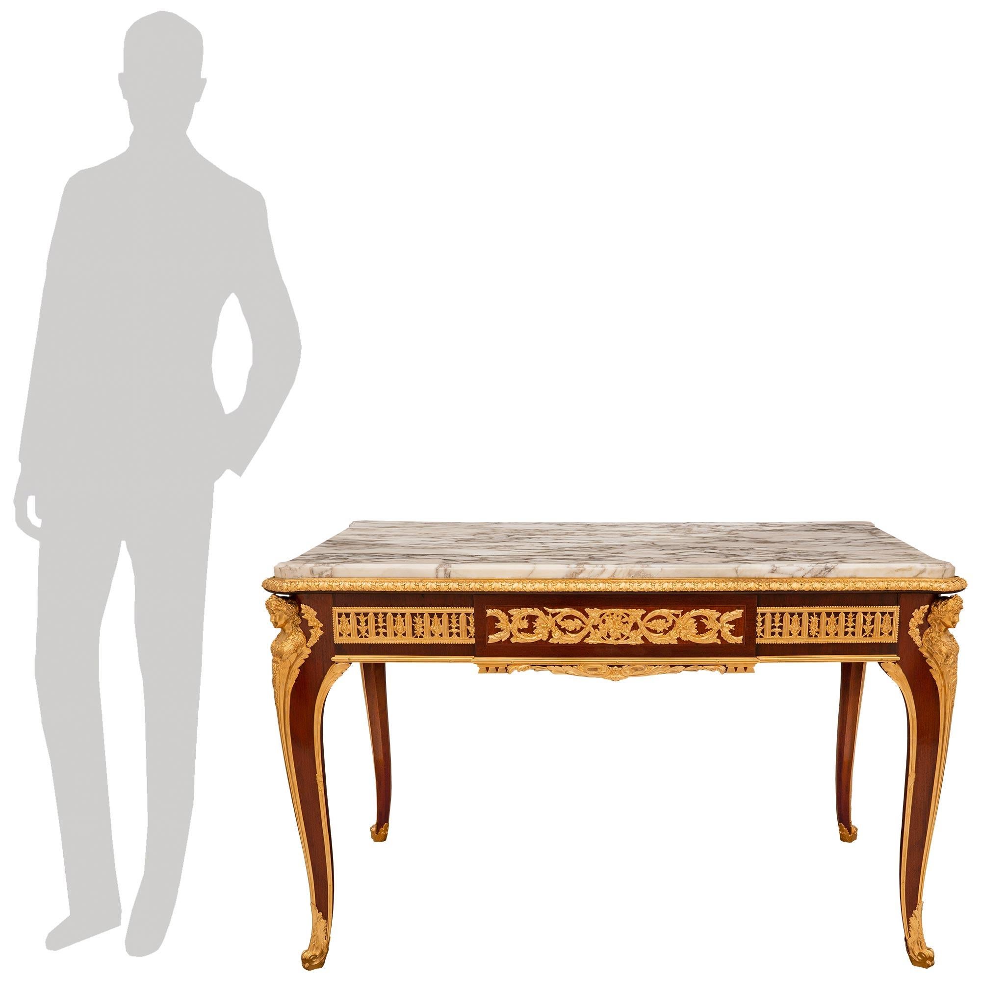 Una splendida ed elegantissima scrivania francese del XIX secolo in mogano, ormolu e marmo Fleur de Pêcher. Questa imponente scrivania rettangolare poggia su quattro gambe cabriole in mogano con decorazioni in Ormolu raffiguranti una bella fanciulla
