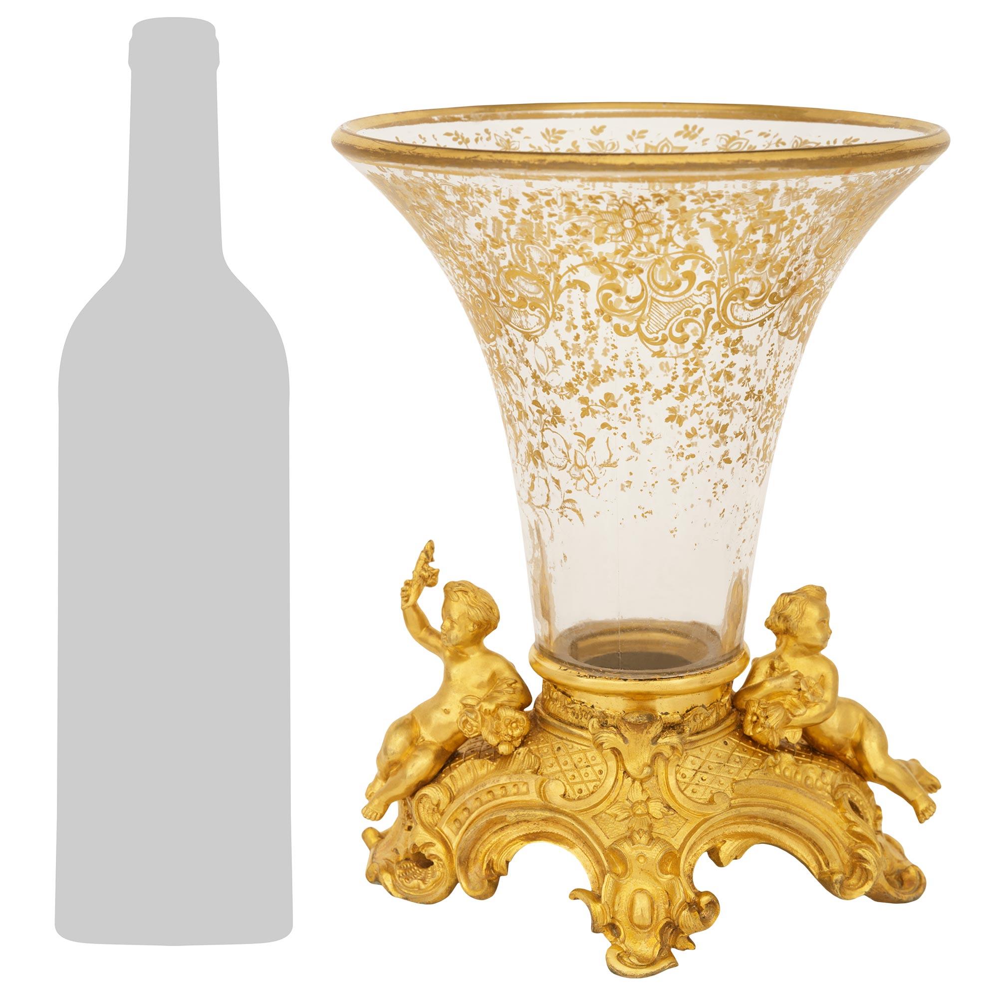 Elegant et très décoratif vase en cristal doré et bronze doré de style Louis XV/XVI du XIXe siècle. Ce superbe vase repose sur une base ovale en bronze doré en forme de C, ornée de rinceaux feuillagés au milieu de motifs en treillis. De part et