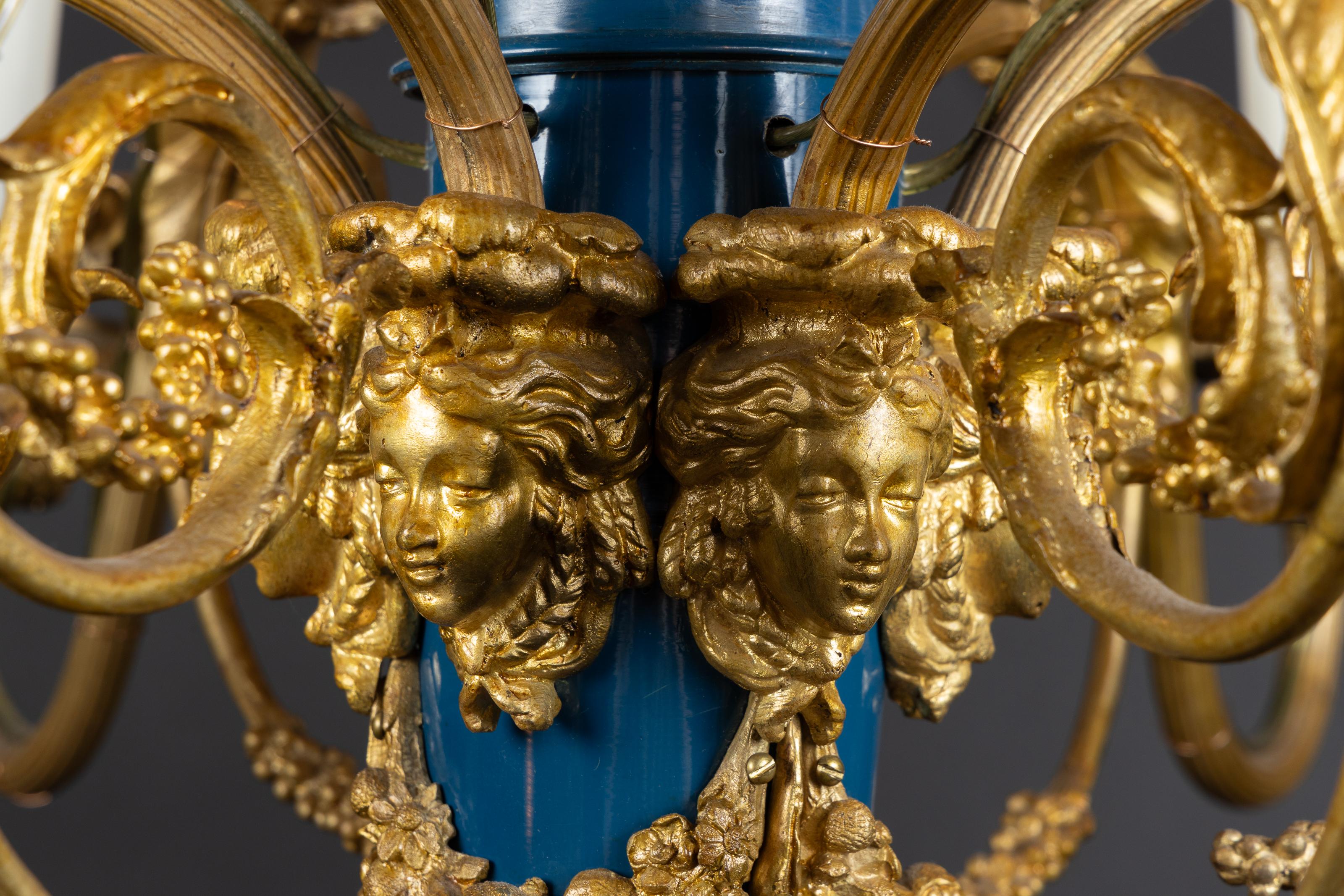 Showcasing a gorgeous Louis XVI chandelier made of bronze, encasing a blue enamel core with herm faces. The French antique piece dates back to 19th century and features a bow ribbon motif crown with rods descending towards the center. A ring of