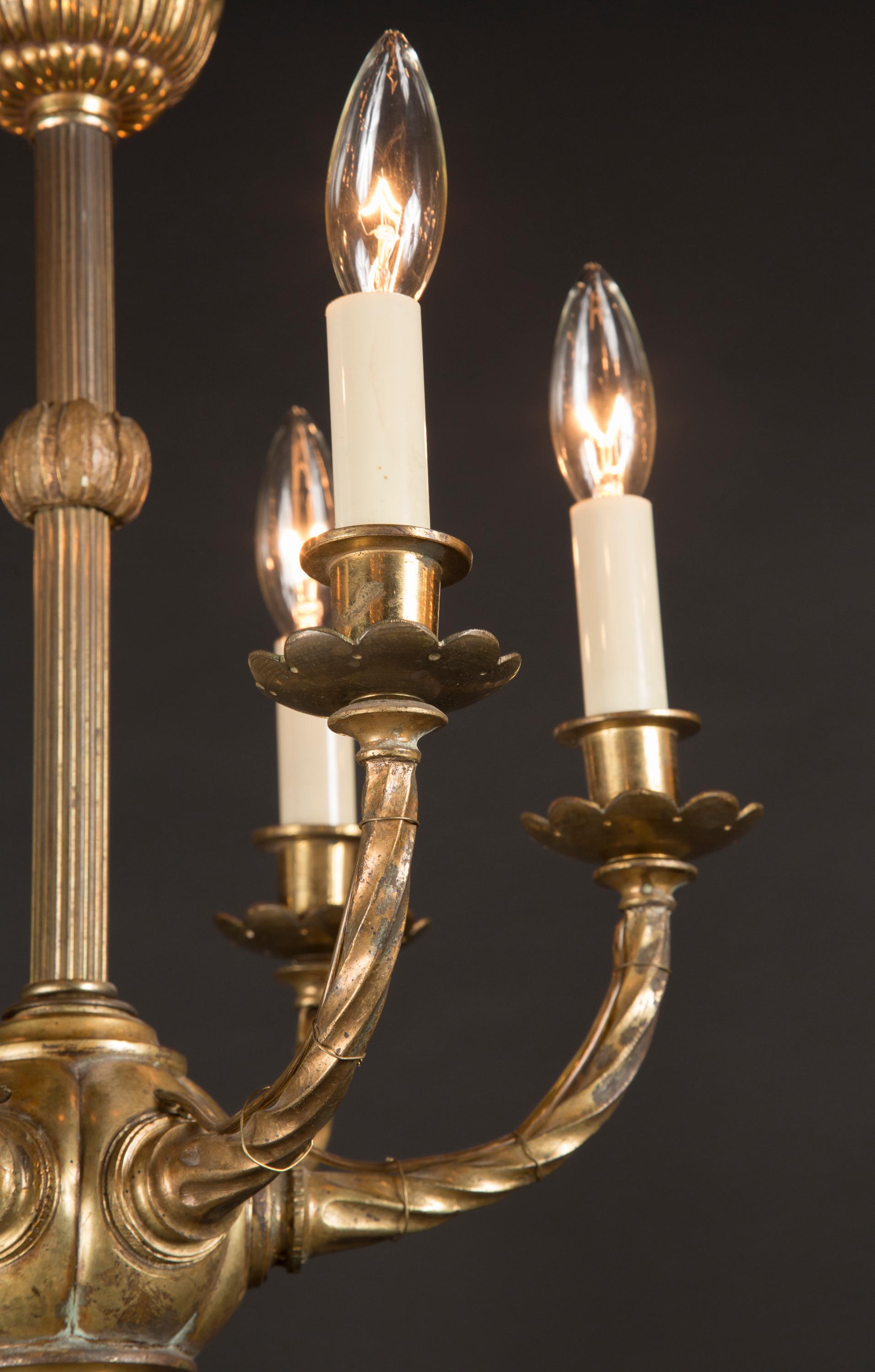 Questo lampadario francese Luigi XVI, splendidamente animato, è realizzato in bronzo fuso e risale al periodo del  XIX secolo. Nota la corona di foglie d'acanto raggruppate, il gambo scanalato, i sei bracci che salgono a spirale verso le semplici