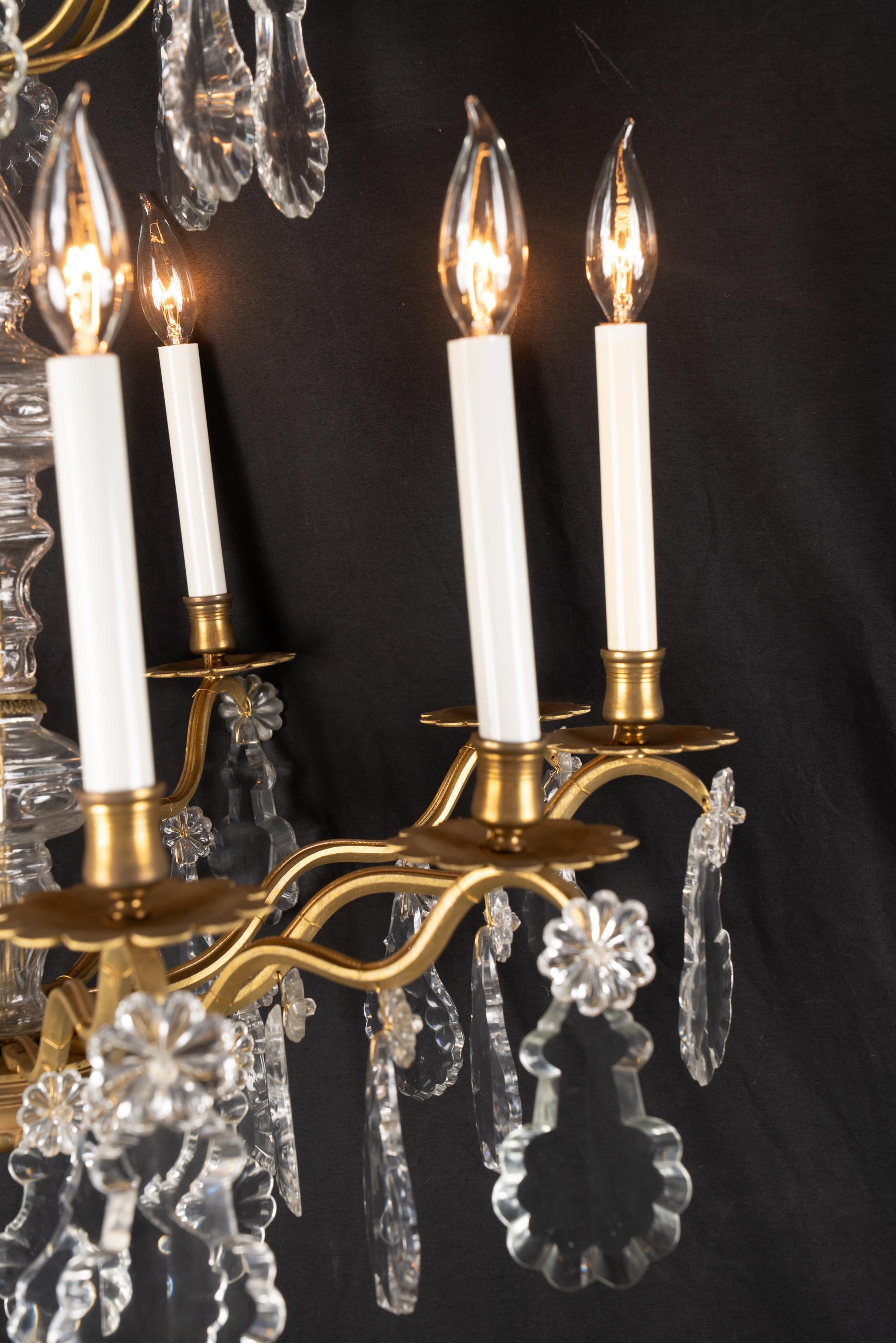 Questo raffinato lampadario francese Luigi XVI del XIX secolo è realizzato in bronzo d'ore e presenta bellissime placchette di cristallo accanto a uno stelo centrale di cristallo. Ciascuna luce poggia su bobeches in bronzo d'ore dai motivi semplici.
