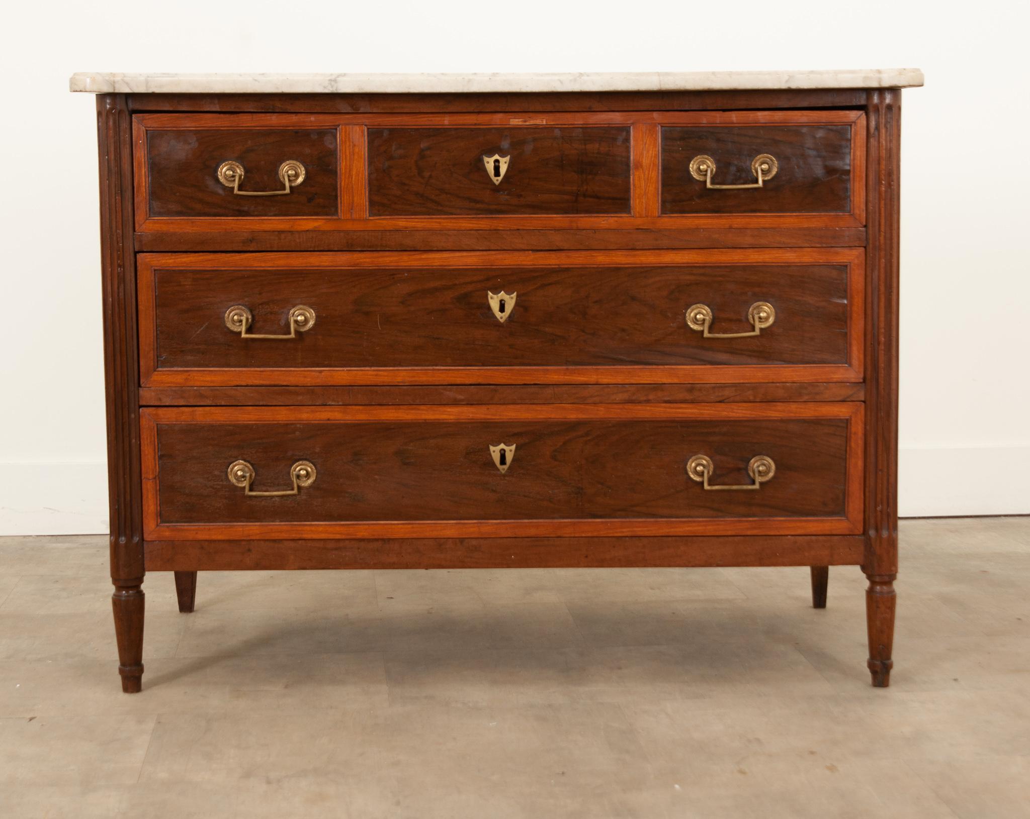 A fine French 19th Century Louis XVI style commode made of beautiful mahogany. Hand-crafted in France circa 1840, its original shaped marble top with beautiful colors and patterns throughout sits over three wide drawers decorated with lustrous brass