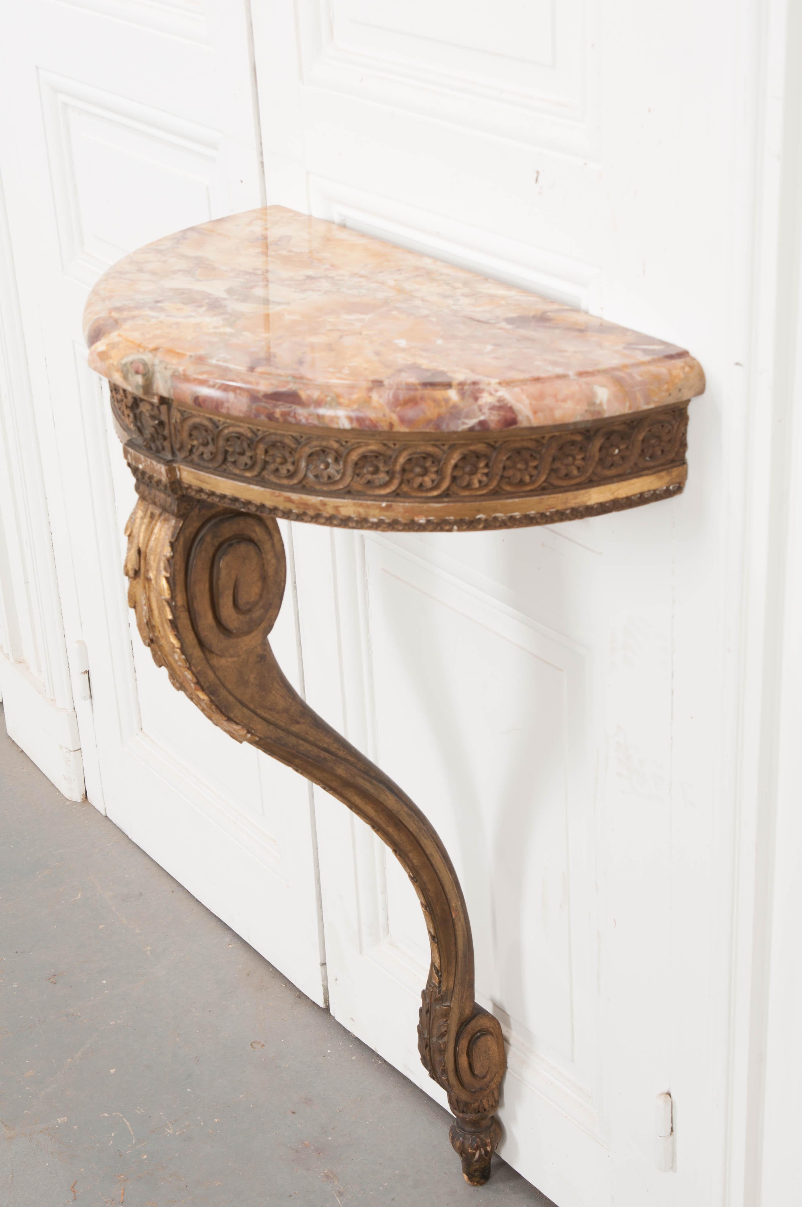 This petite Louis XVI-style wall-mounted demilune console table, circa 1860s, is from France and has a wonderful patina! Featuring a gorgeous rouge marble top with gold inclusions and highlights, over a floral-and-scroll carved apron resting on a