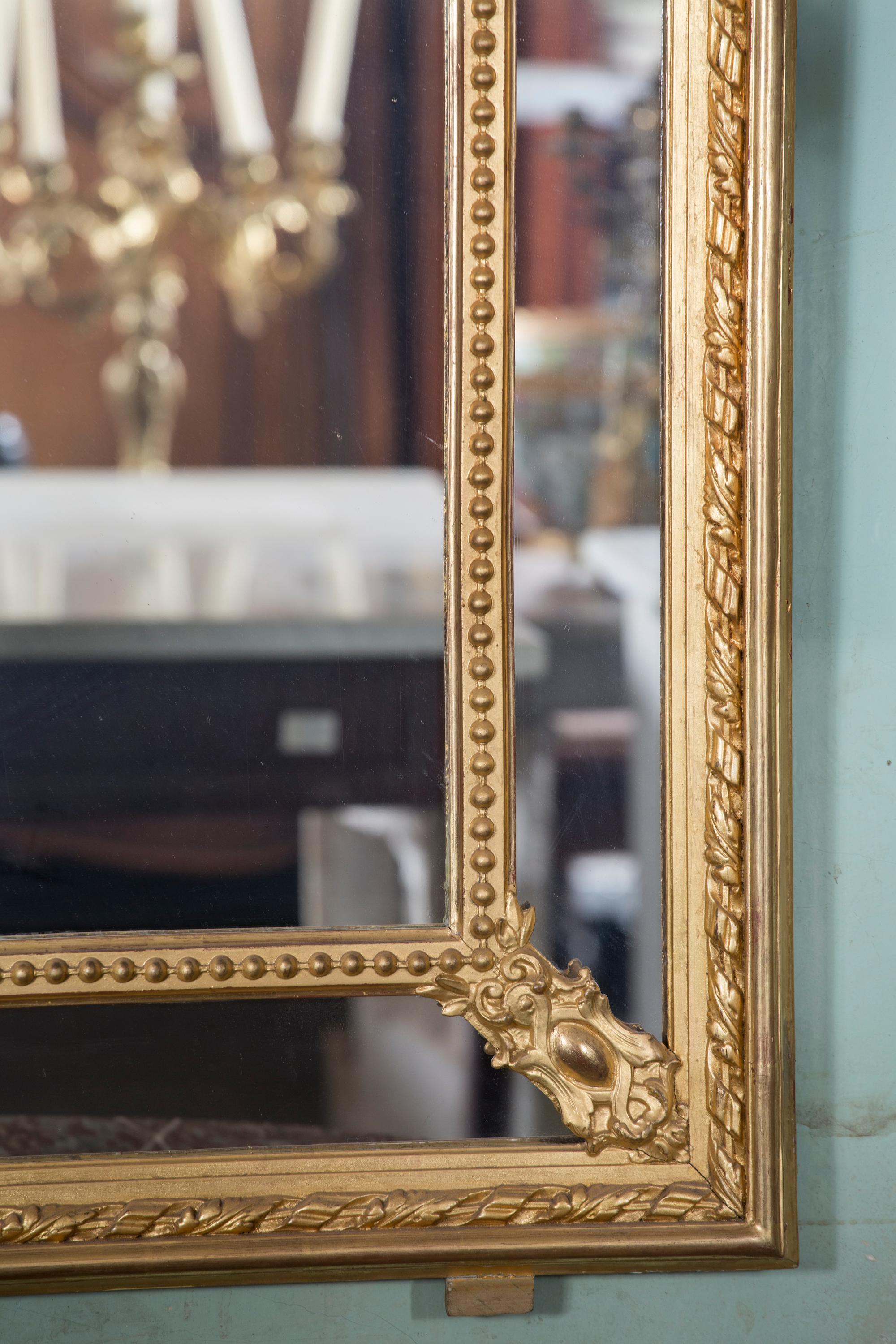 Questo splendido specchio rettangolare Luigi XVI è foderato d'oro e risale al XIX secolo, circa al 1860. Il pezzo è una combinazione di legno dorato e dorato-gesso. La parte superiore dell'opera presenta una coppia di figure maschili e femminili