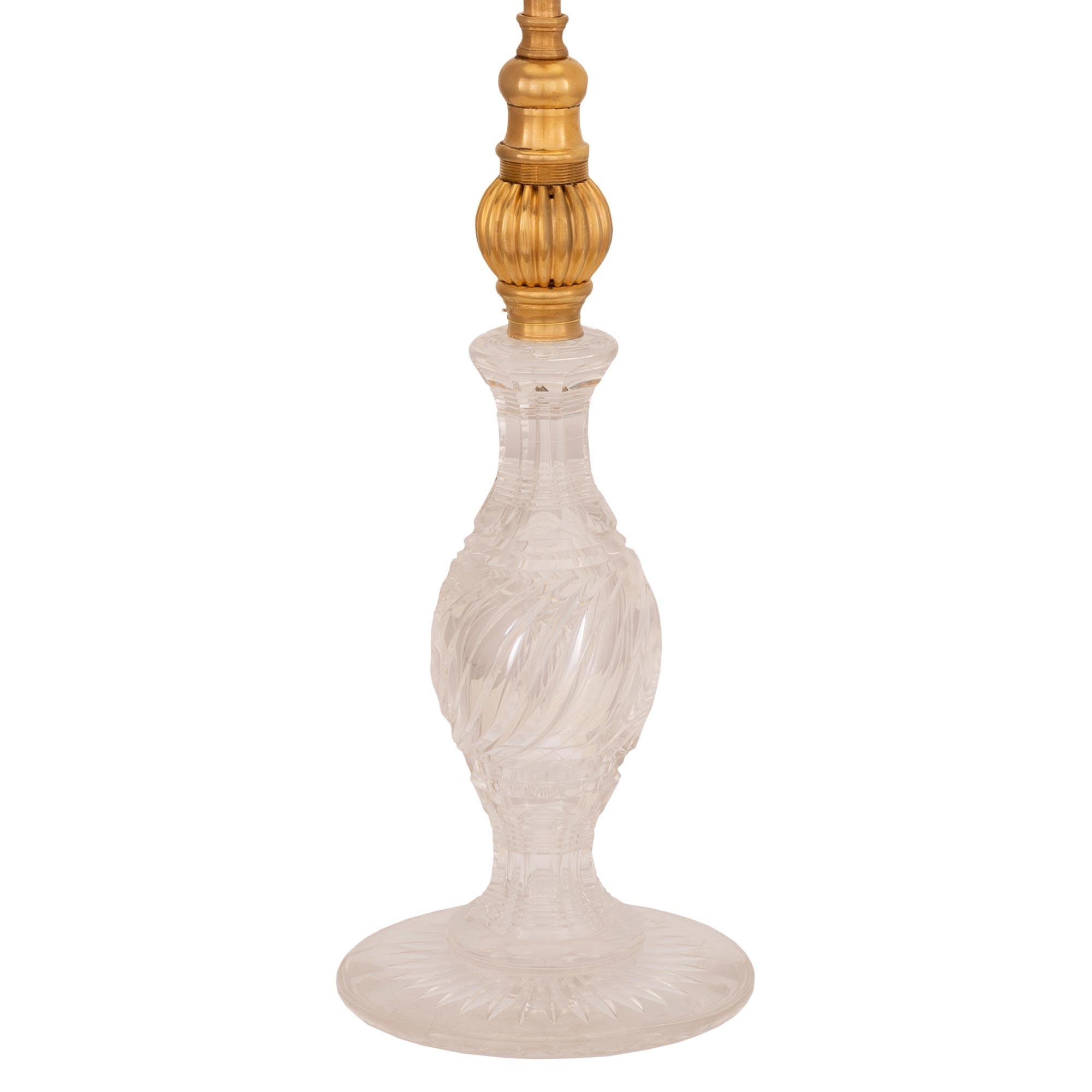 Une charmante lampe française du 19ème siècle, de style Louis XVI, en cristal de Baccarat et bronze doré. La lampe est surélevée par un corps en cristal de Baccarat très décoratif, avec une base circulaire feuillagée et un magnifique support central