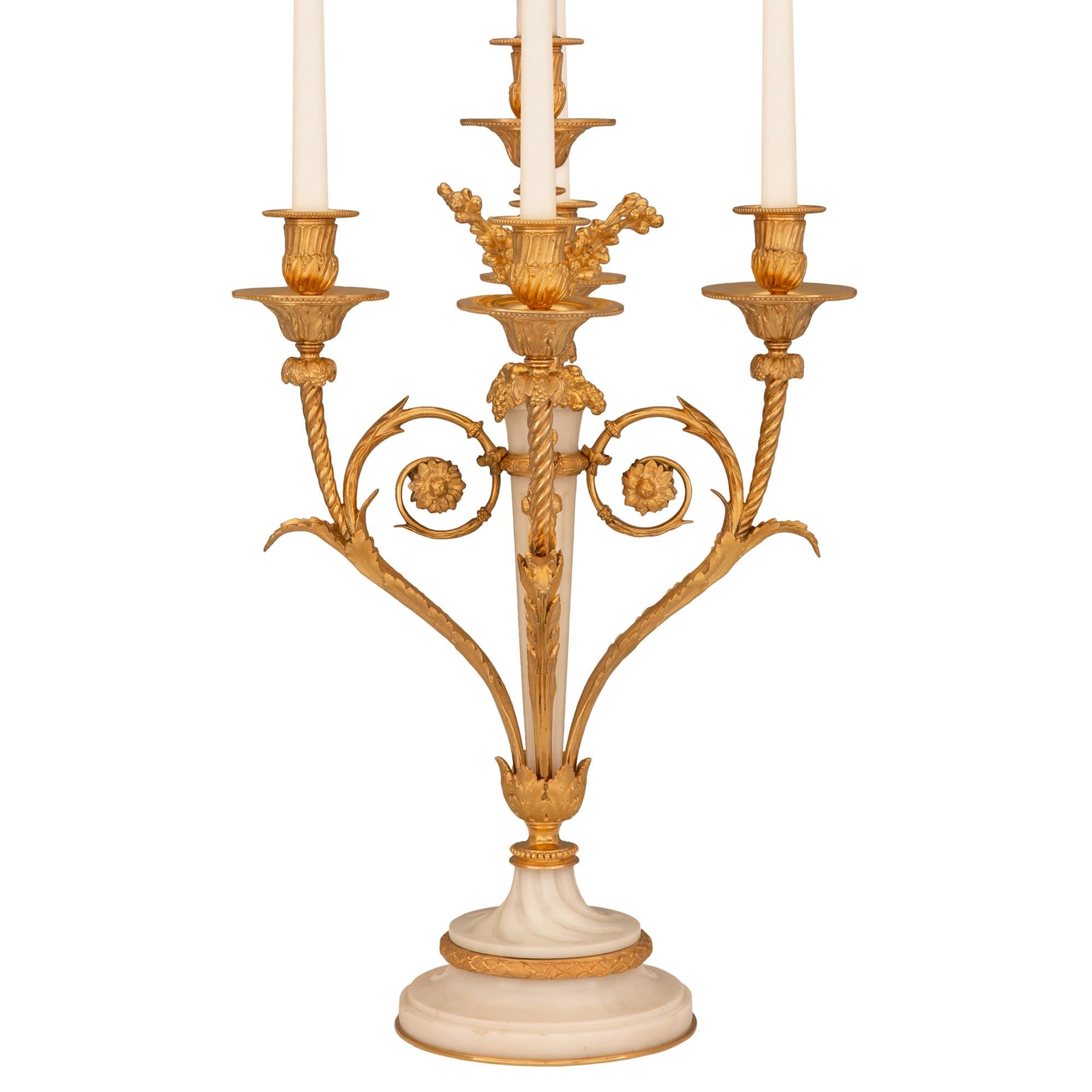 A striking and extremely decorative French 19th century Louis XVI st. Belle Époque period candelabra lamps after a model by Pierre Gouthière. Each four arm lamp is raised by an elegant circular white Carrara marble base with a fine bottom ormolu
