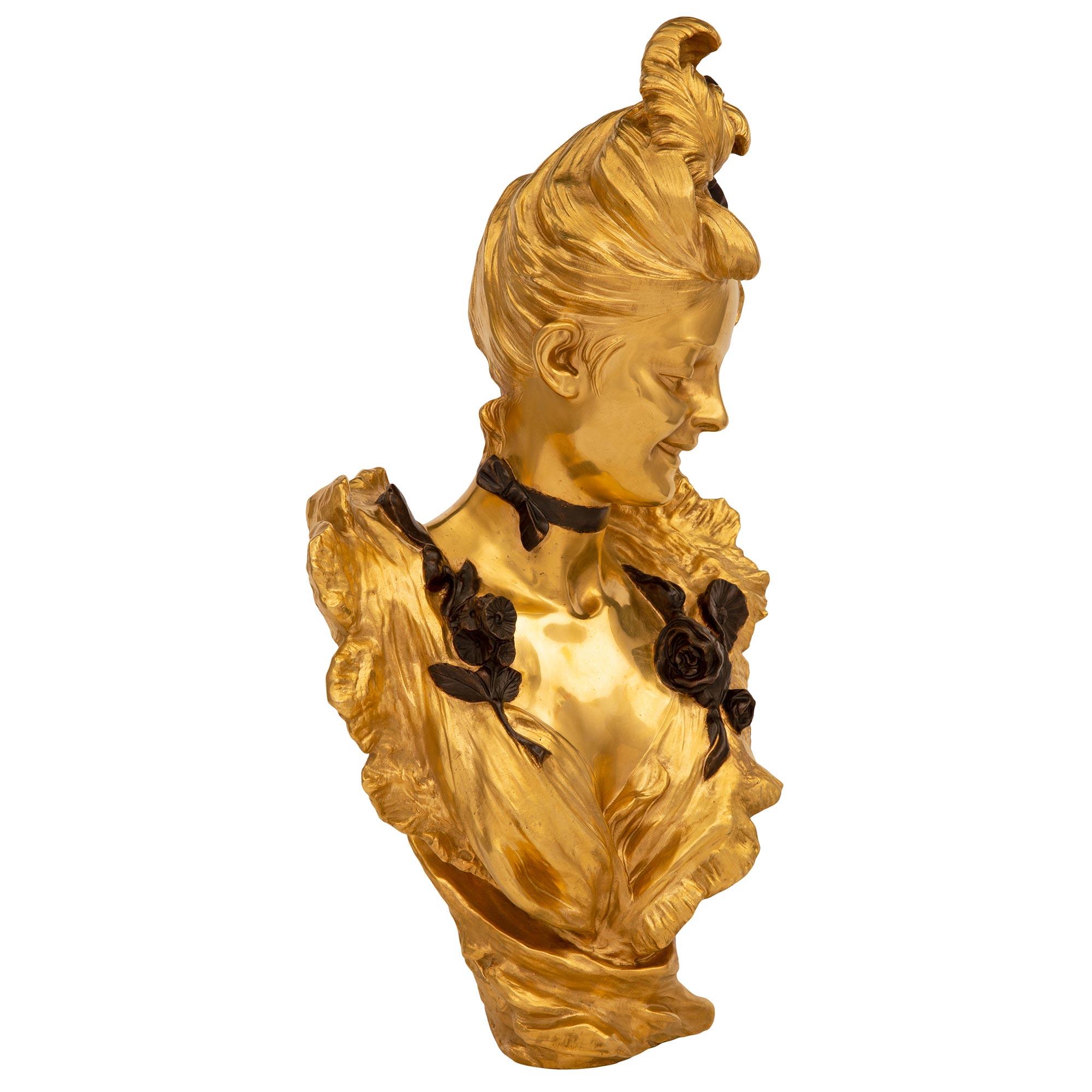 Exceptionnel et très élégant buste d'une belle jeune fille en bronze doré et patiné, d'époque Louis XVI et Belle Époque, signé V. Bruyneel. Le buste est surélevé par un vêtement fluide merveilleusement exécuté qui remonte autour des épaules de la
