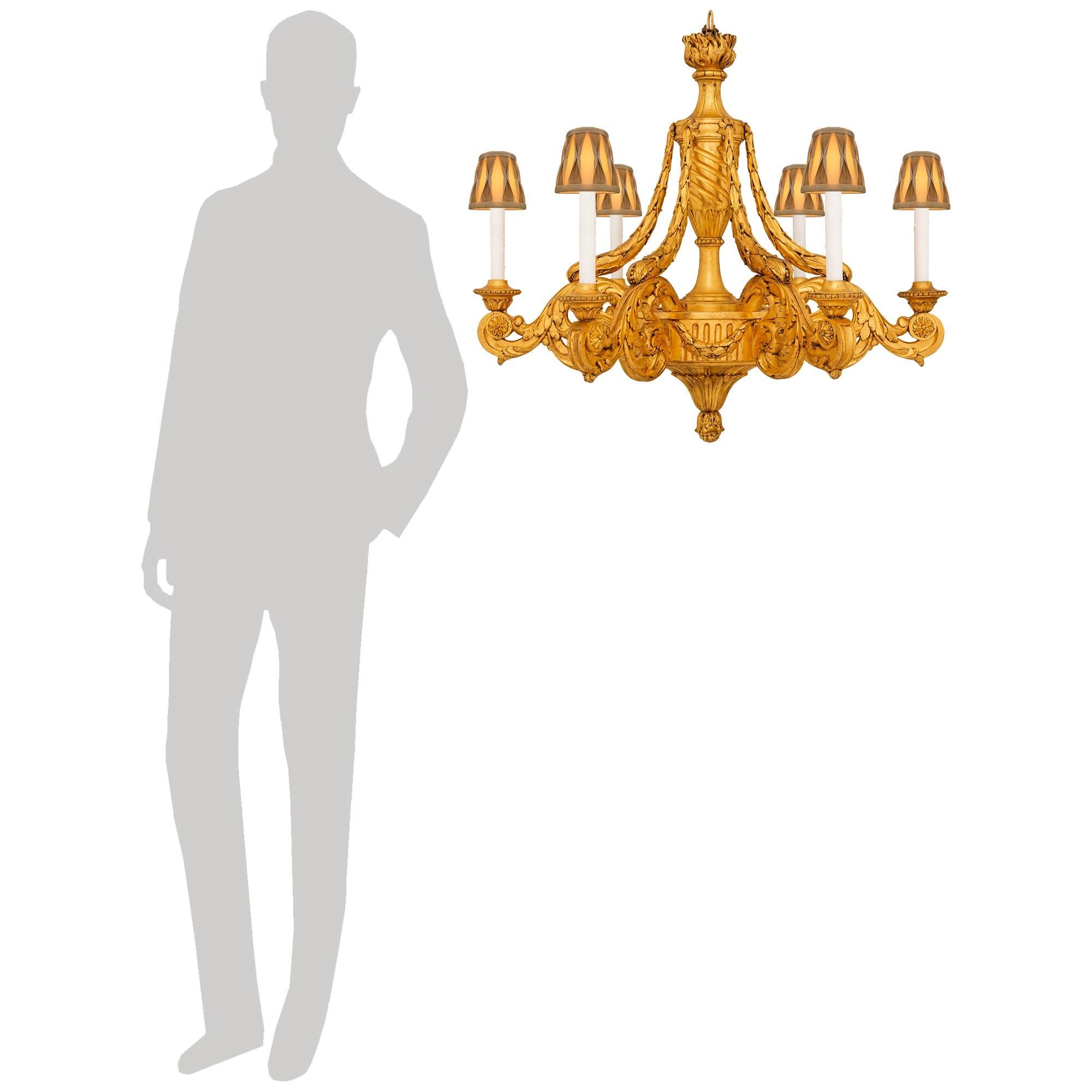 Un elegantissimo lampadario a sei bracci in legno dorato circolare del XIX secolo Luigi XVI. Il lampadario è dotato di un terminale inferiore a bacche sotto una fascia centrale a bacche decorata da ghirlande di alloro a bacche. I bracci a 