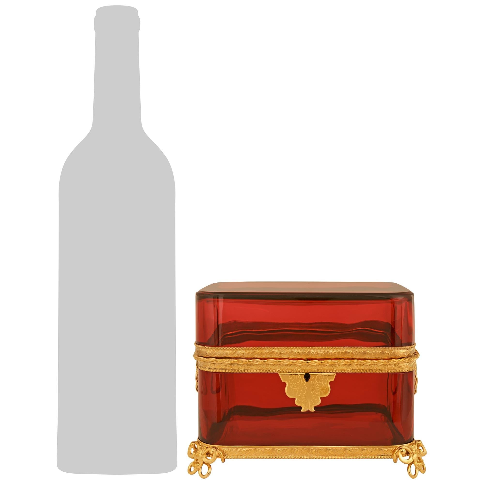 Ein charmantes und elegantes französisches Kästchen aus Preiselbeerglas und vergoldetem Metall aus dem 19. Jahrhundert im Stil Louis XVI. Der wunderbare quadratische Kasten mit Deckel wird von vier schmetterlingsförmigen Füßen aus vergoldetem Metall