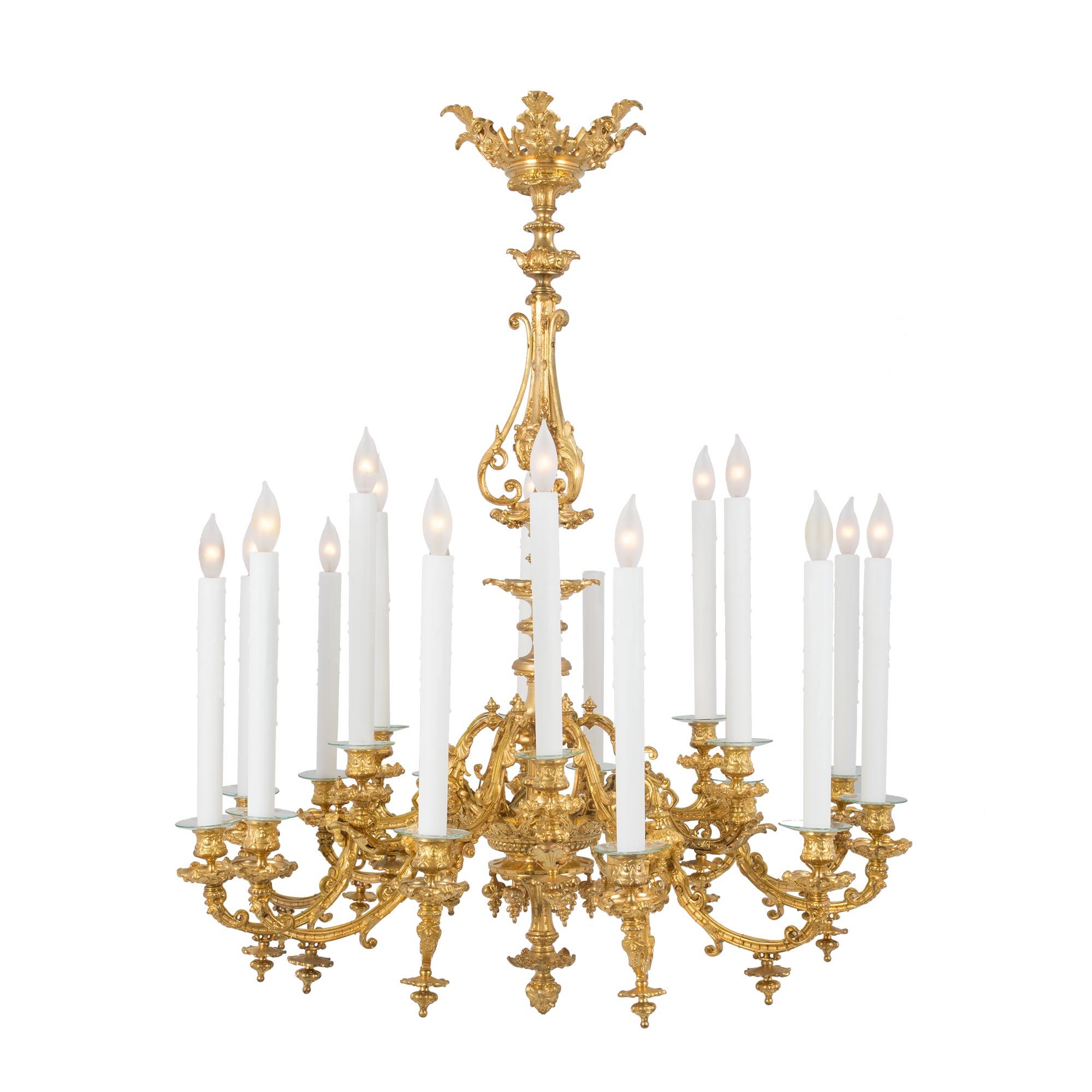 An elegant French 19th century Louis XVI st. eighteen light ormolu chandelier. A regal pierced crown with acanthus leaf and rosette designs tops the tiered pedestal fut. An urn shaped element displaying mask medallions with hammered background is