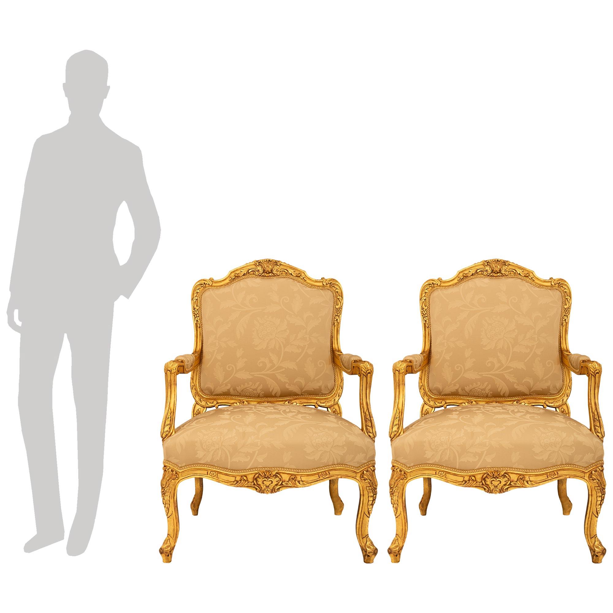 A stunning and most elegant pair of French 19th century Louis XV st. Giltwood armchairs. Each beautiful chair is raised on four cabriole legs with foliate carvings. The front apron is designed with an arbalest shaped scrolling foliate central