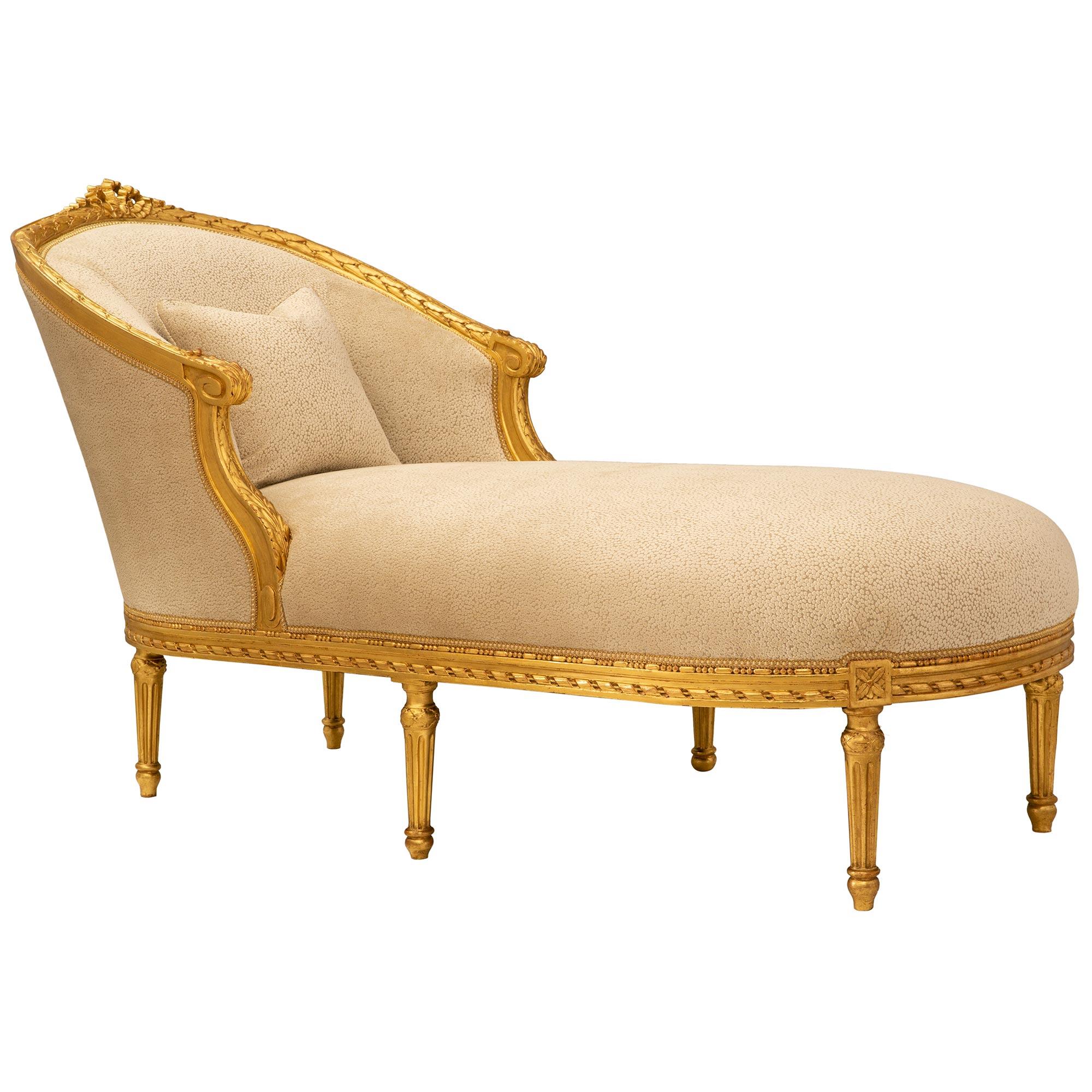 An exceptional and most elegant French 19th century Louis XVI st. Giltwood chaise lounge settee. The oval shaped chaise is raised by six elegant tapered fluted legs with top carvings of acanthus leaves. The straight apron is decorated with carved