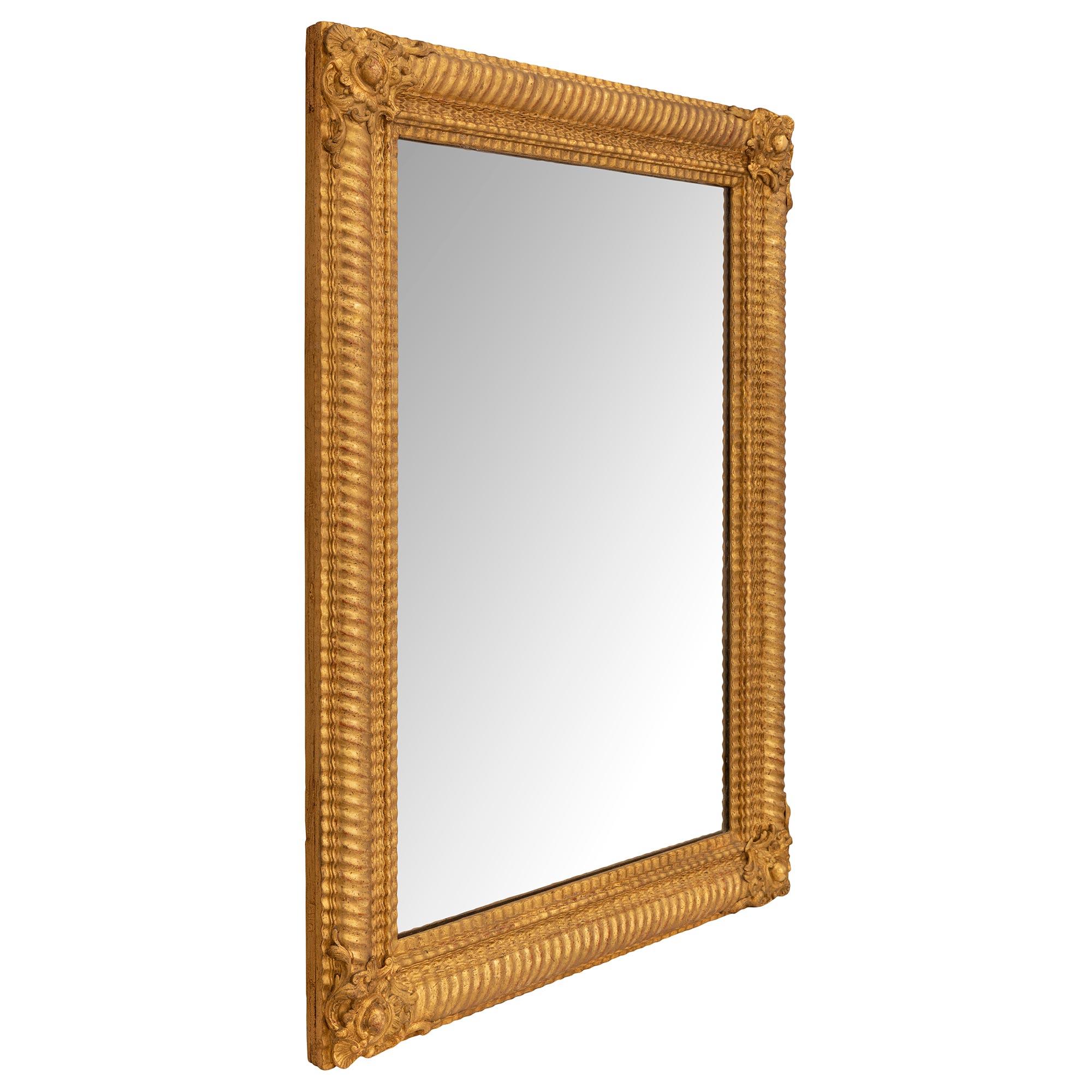 Deliziosa specchiera francese del XIX secolo in legno dorato di stile Luigi XVI. Lo specchio di forma rettangolare conserva la lastra originale incastonata in una bella cornice in legno dorato screziato con movimenti decorativi a onda e a gadroon in