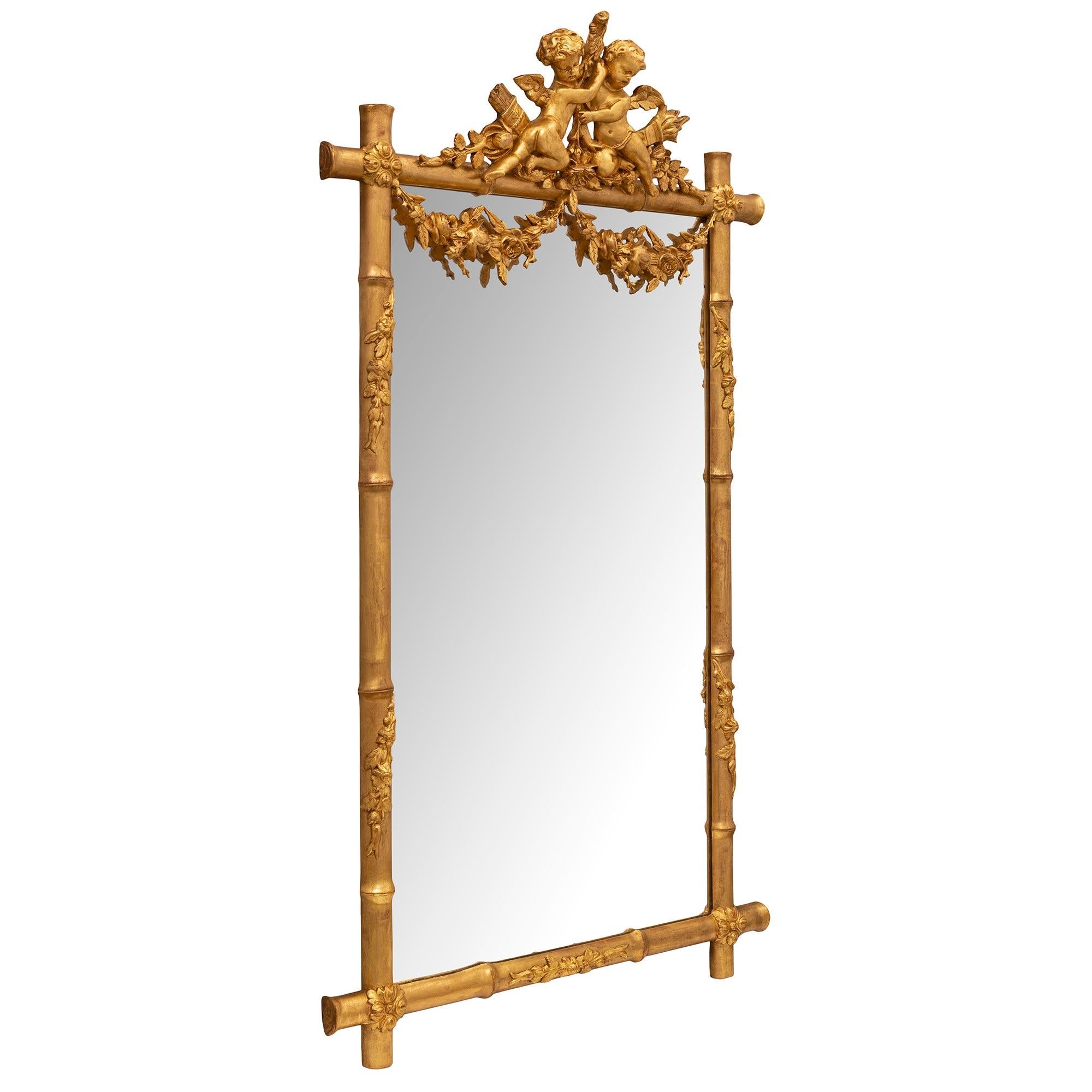 A most decorative French 19th century Louis XVI st. giltwood mirror. The mirror is set within a beautiful bamboo designed frame tied by charming rosettes and adorned with wrap around vine like branches. The top crown is centered by two cherubs