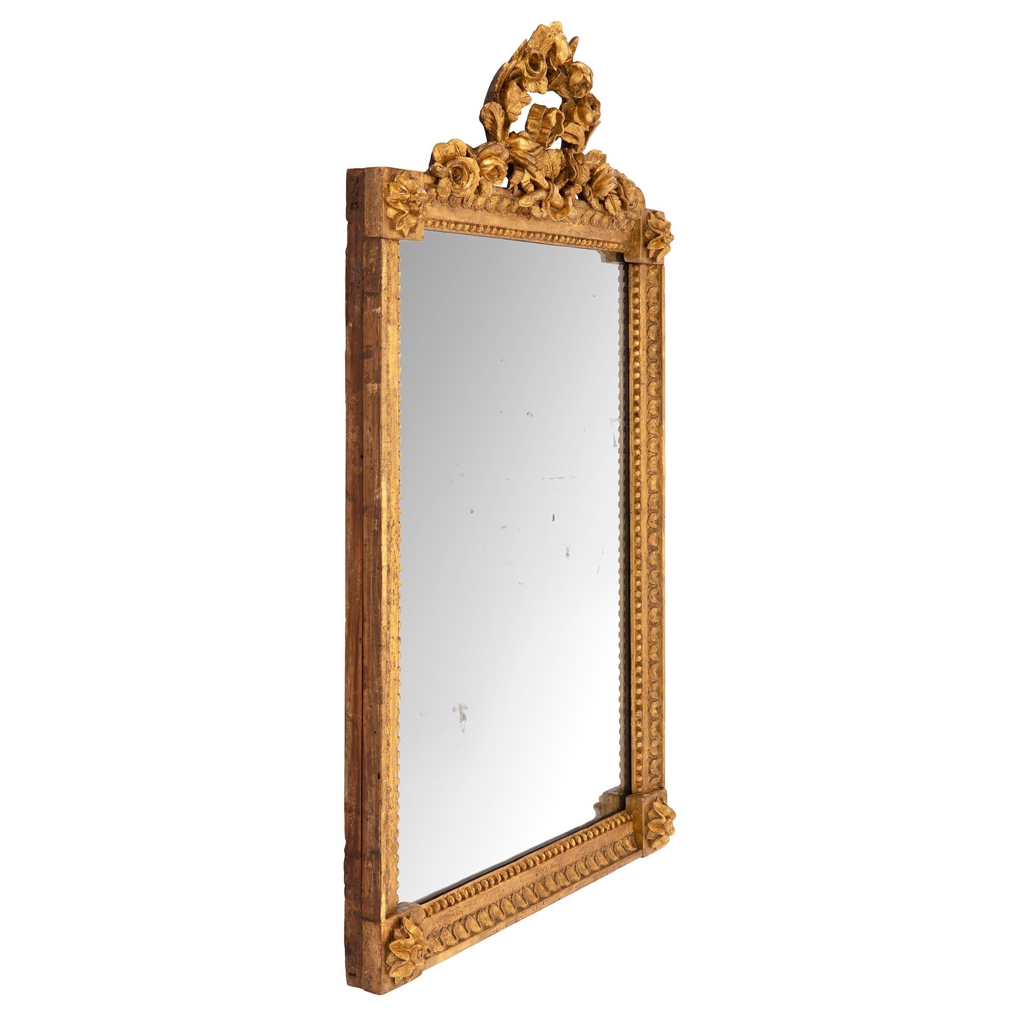 A charming French 19th century Louis XVI st. giltwood mirror. The mirror retains its original mirror plate set within a straight frame with a lovely beaded and foliate wrap around band with delicate block rosettes at each corner. The beautiful top