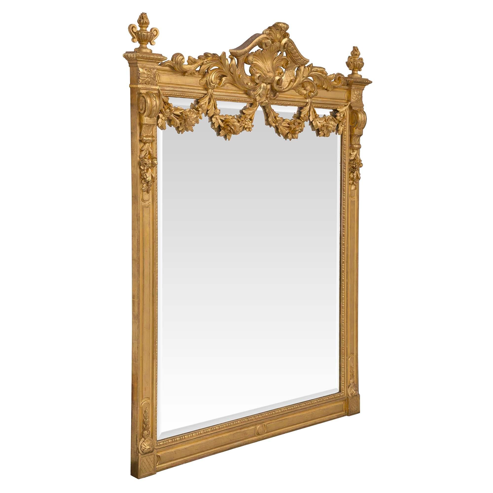 A magnificent French 19th century Louis XVI st. giltwood mirror. The original beveled mirror plate is framed within a decorative beaded design. The frame displays a circular bottom central reserve and block rosettes at each corner with a lattice