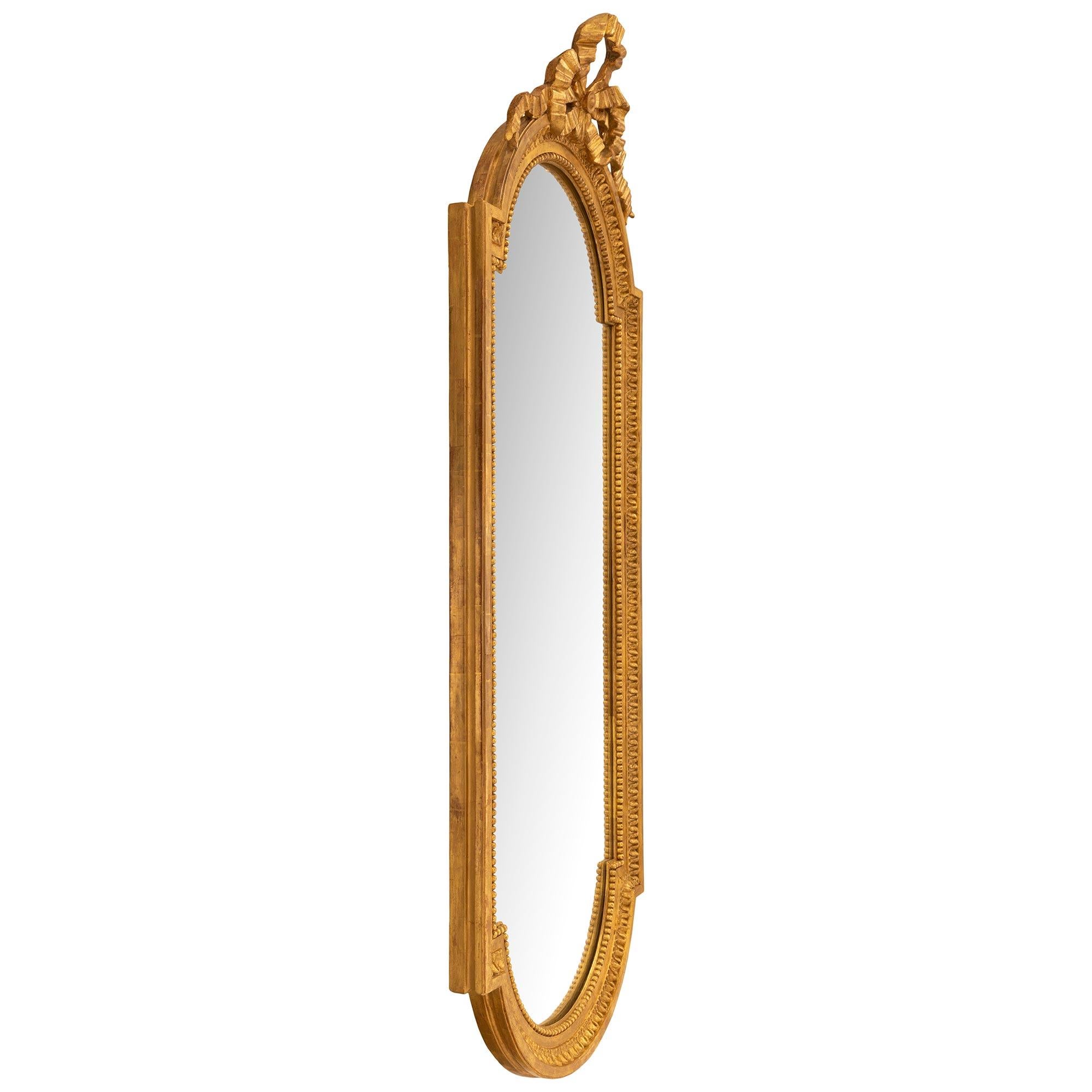 An elegant and unique French 19th century Louis XVI st. Giltwood mirror. The original mirror plate is framed within an elongated Giltwood band with inner beaded and outer Coeur de Rai designs all in a rich satin and burnished finish. The top and