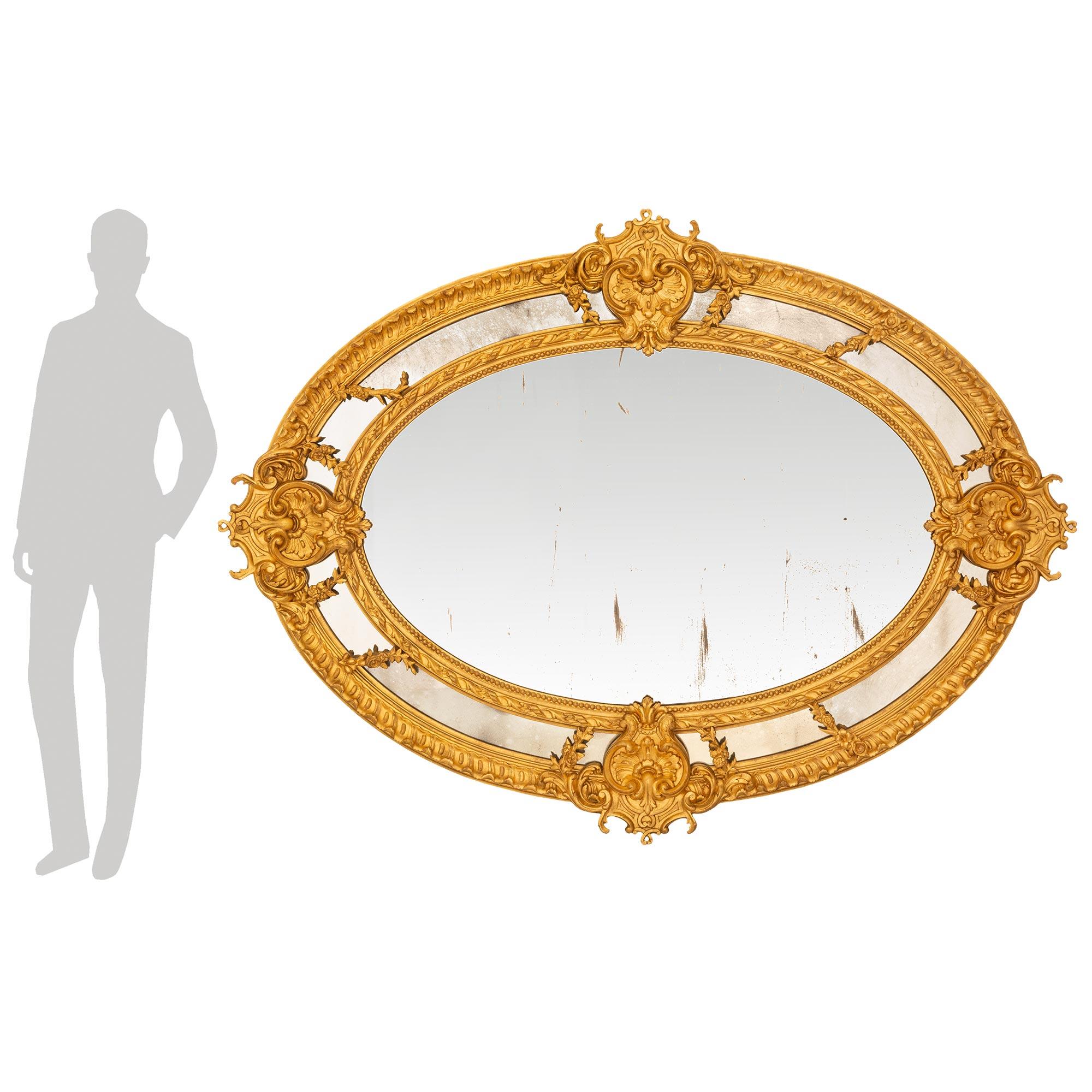 Miroir monumental de grande qualité en bois doré de style Louis XVI du XIXe siècle. Ce miroir ovale à double encadrement présente ses plaques de miroir d'origine et est encadré d'une fine bordure perlée et d'un bandeau de feuillage torsadé. Les