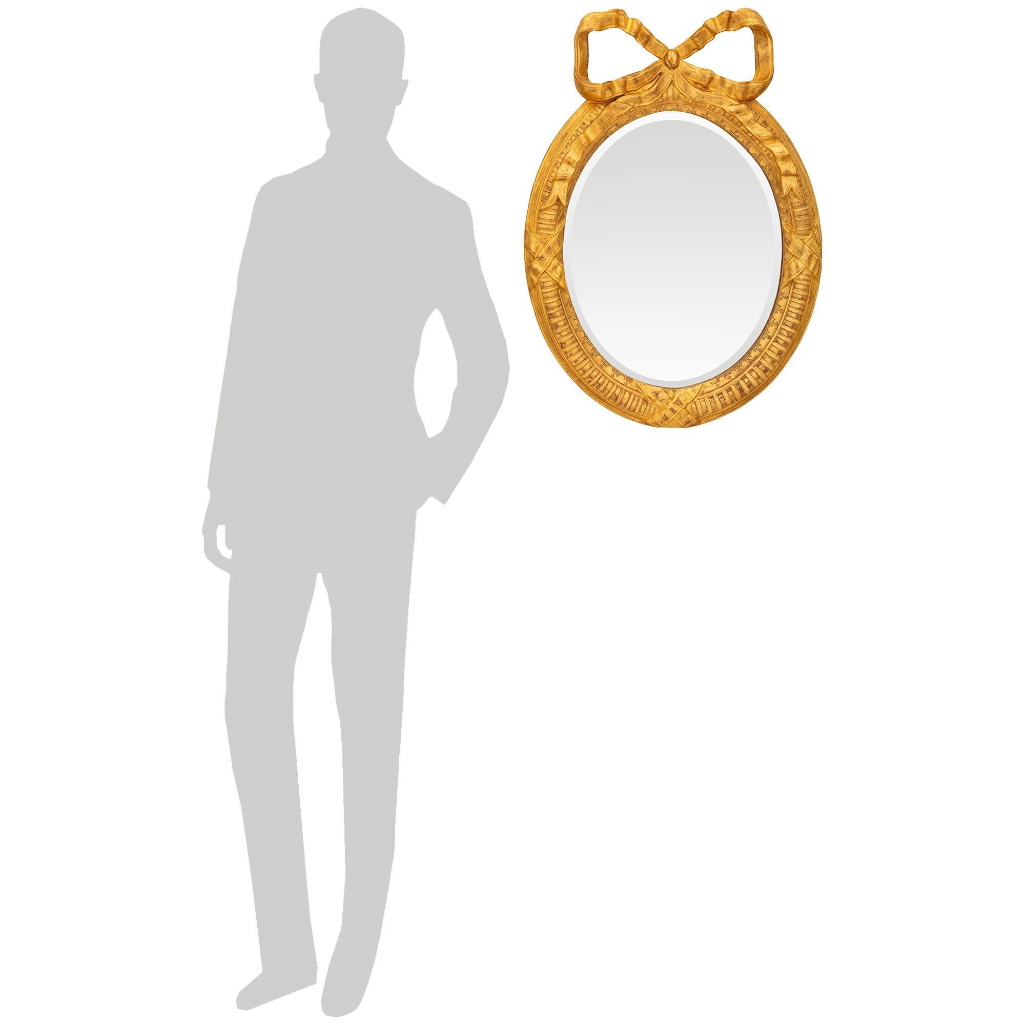Charmant miroir de grande qualité en bois doré de style Louis XVI du XIXe siècle. Ce magnifique miroir ovale présente sa plaque de miroir biseautée d'origine, entourée d'un bandeau cannelé intérieur. Des réserves en forme de X soulignent le bas et