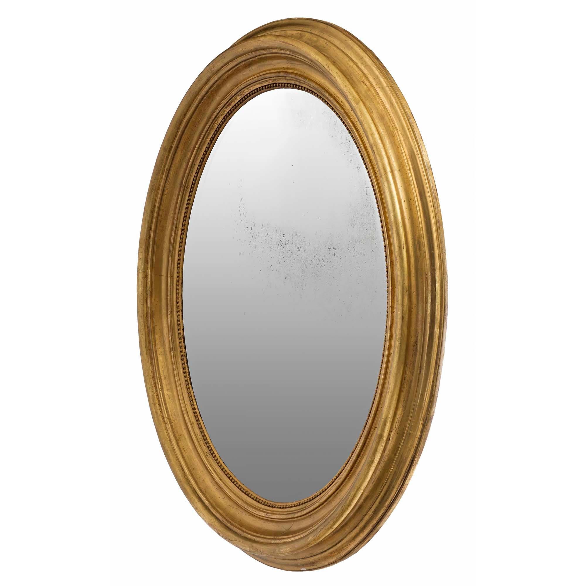Très beau miroir ovale en bois doré de style Louis XVI du XIXe siècle. La plaque de miroir originale est insérée dans un cadre en bois doré satiné et bruni. L'impressionnant cadre moucheté présente une bordure intérieure perlée. Le miroir peut être
