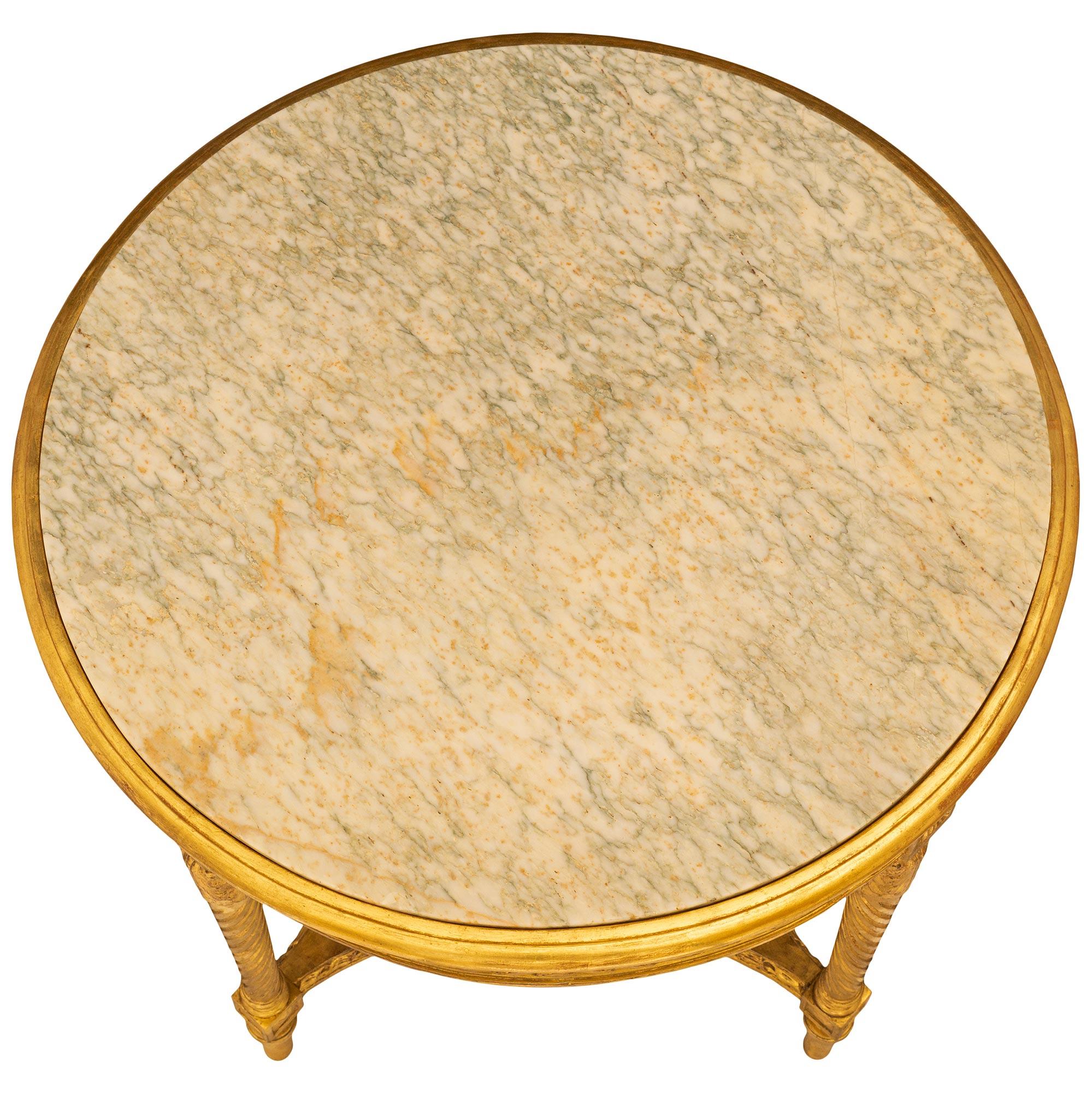 Table d'appoint en bois doré de style Louis XVI du 19e siècle, délicieusement décorée. Cette table circulaire élégante et très détaillée est soutenue par quatre pieds circulaires effilés avec une bande supérieure. Les quatre pieds sont reliés par un