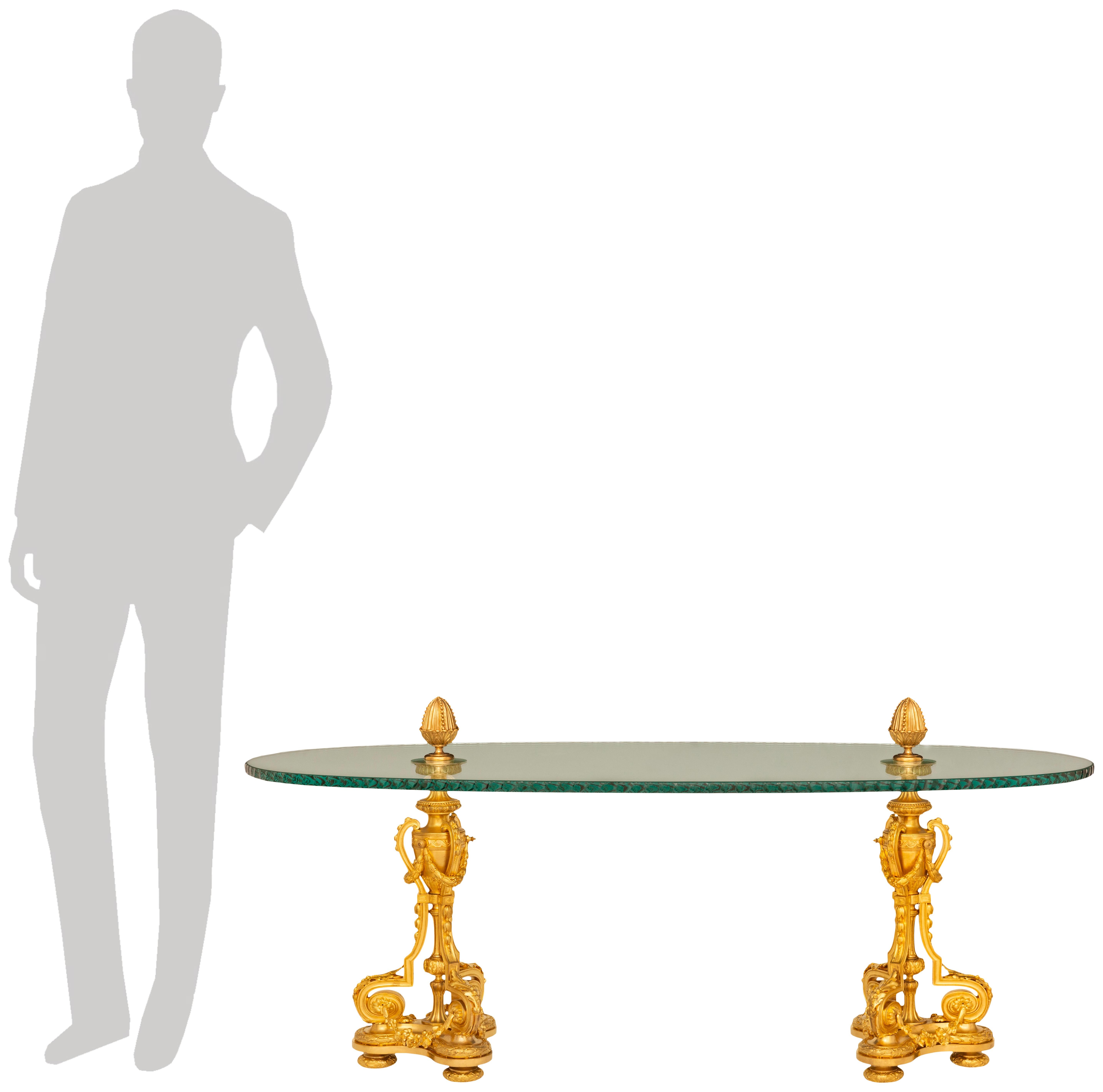 Très élégante table basse en verre et bronze doré de style Louis XVI du XIXe siècle. Cette superbe table repose sur deux pieds triangulaires aux côtés concaves et aux extrémités arrondies. Chaque jambe large est soutenue par des pieds circulaires en