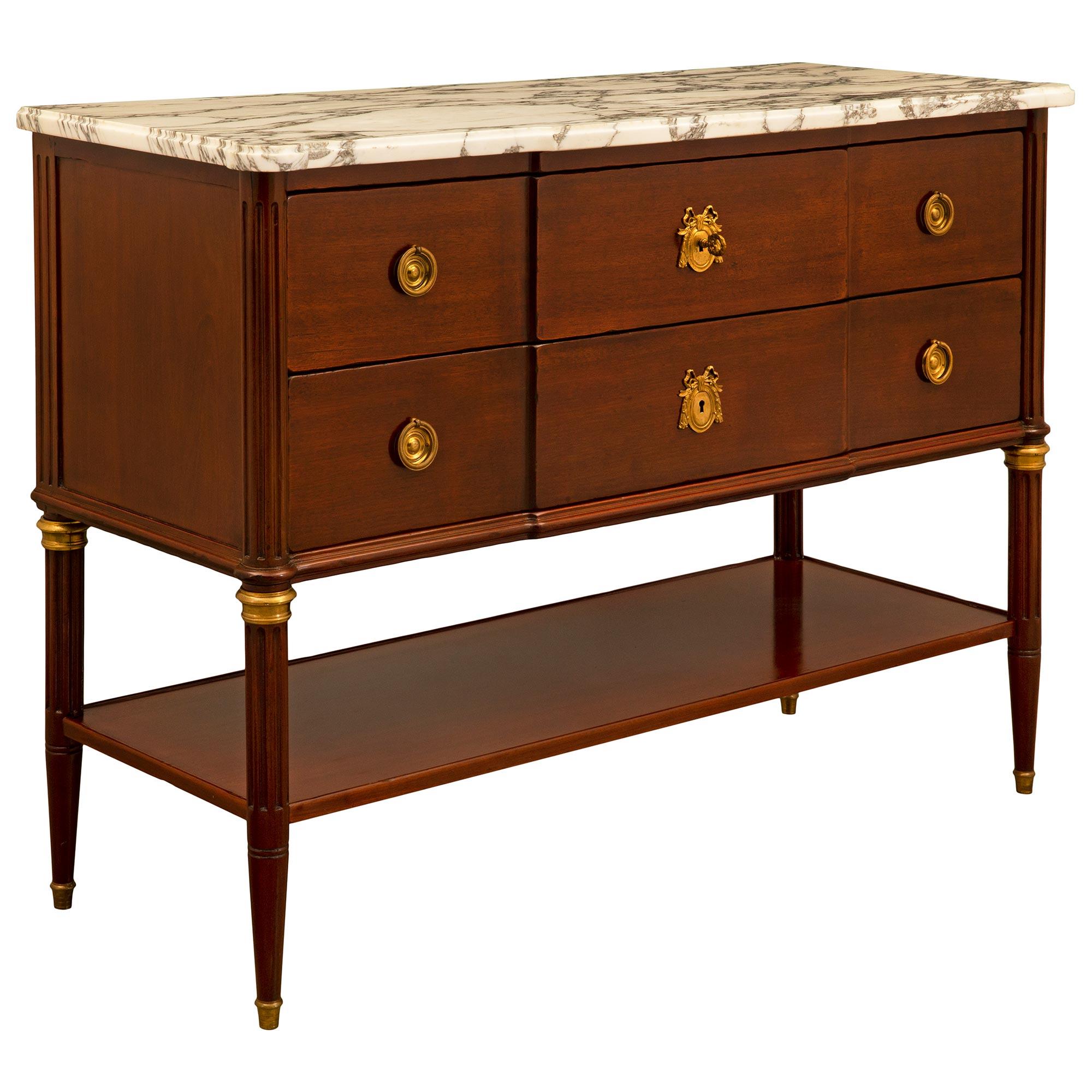 An elegant French 19th century Louis XVI st. mahogany commode. The chest is raised by circular tapered fluted legs with fine ormolu sabots and top caps. Each leg is connected by a mahogany bottom tier with a raised edge. Above a mottled carved