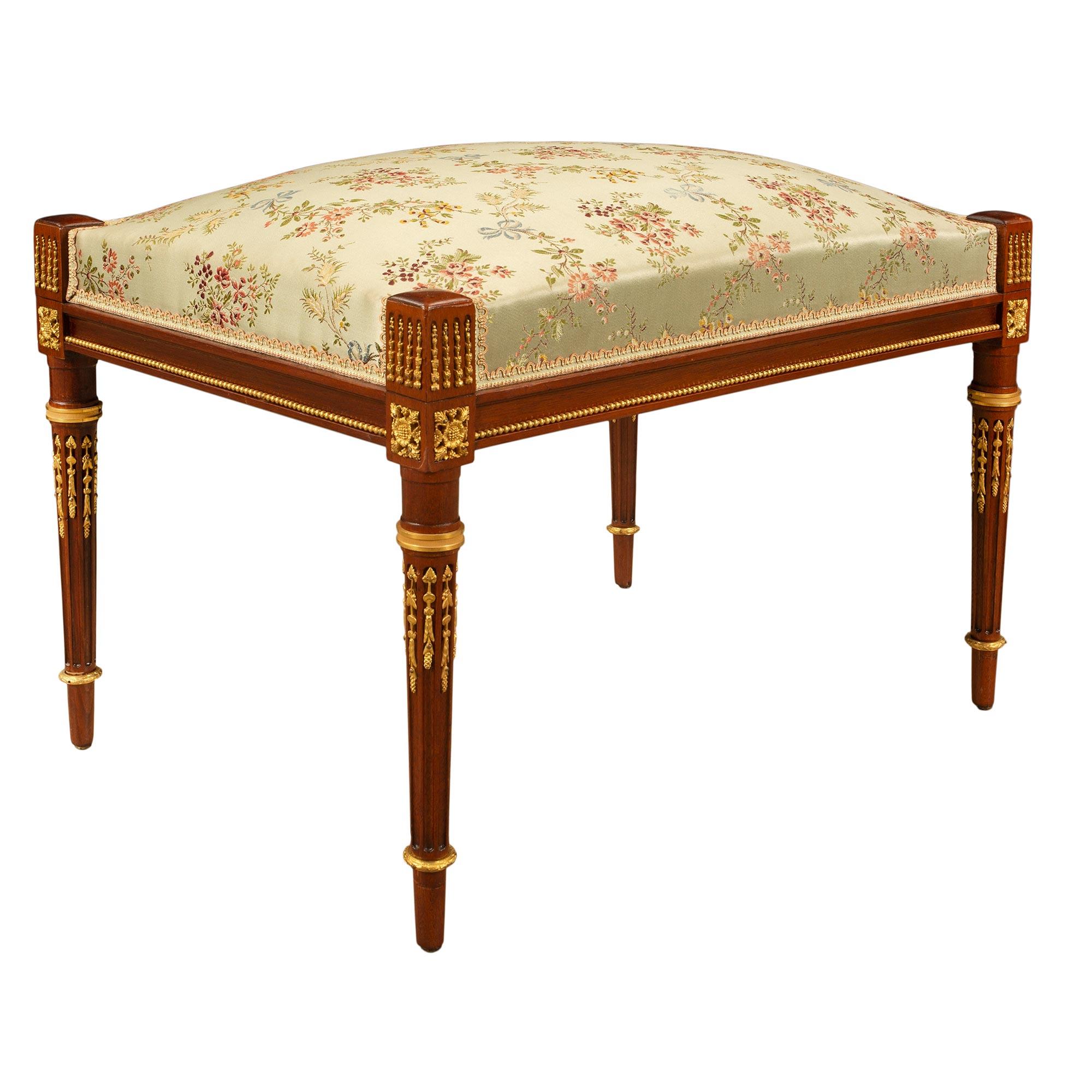 An extremely elegant and high quality French 19th century Louis XVI st. mahogany and ormolu bench. The bench is raised by slender circular tapered fluted legs with richly chased fitted ormolu chandelles and mottled top caps. Above each leg are