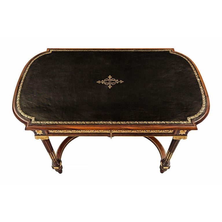 A stunning French 19th century Louis XVI st. mahogany and ormolu center table / desk. The table is raised on topie feet below an ormolu rosette block and reeded supports with ormolu chandelles, topped by ormolu scrolled capitols. The supports are