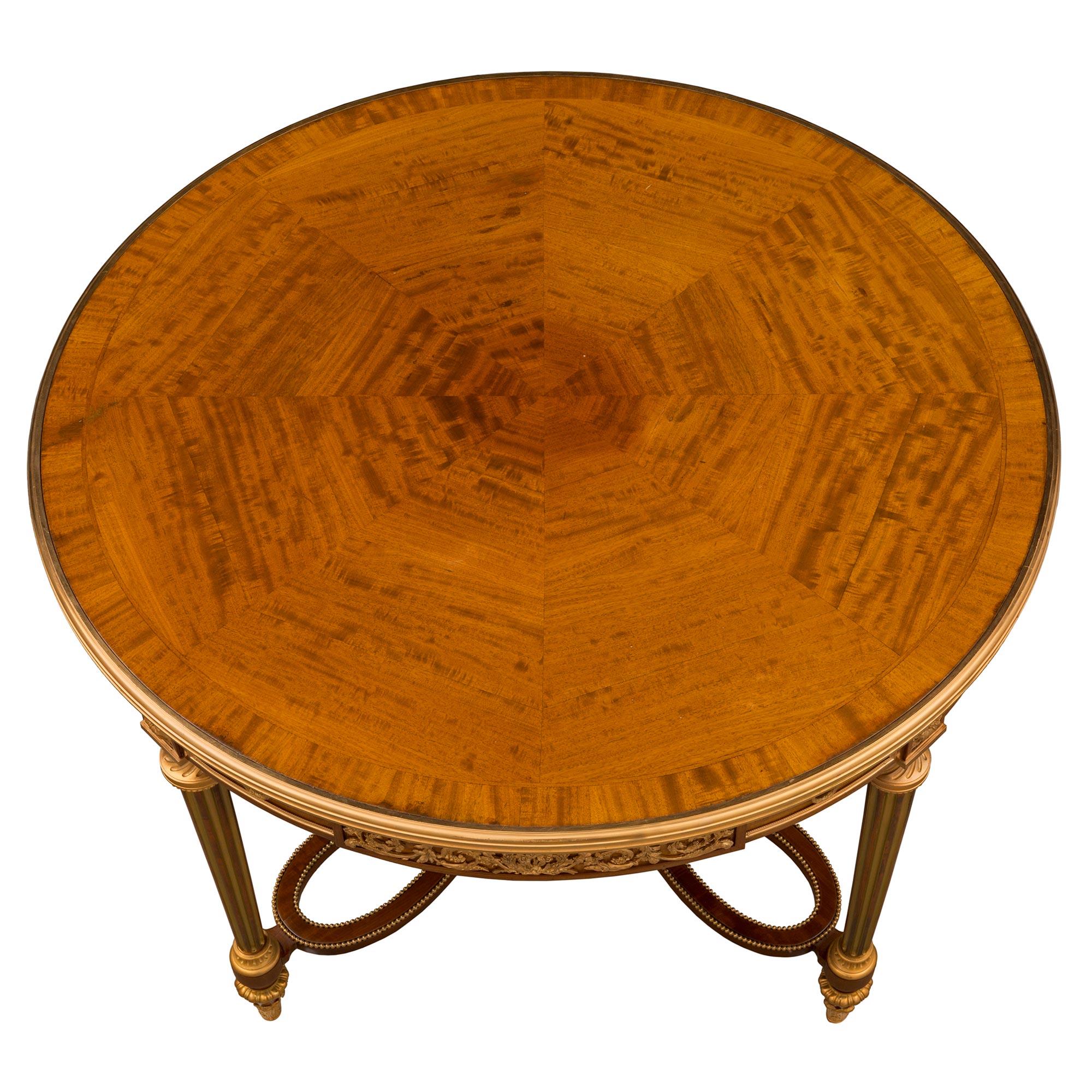 A stunning and very high quality French 19th century Louis XVI st. Mahogany, Satinwood, and ormolu center table attributed to Henry Dasson. The circular table is raised by delicate topie shaped feet with beautiful fitted foliate ormolu sabots and