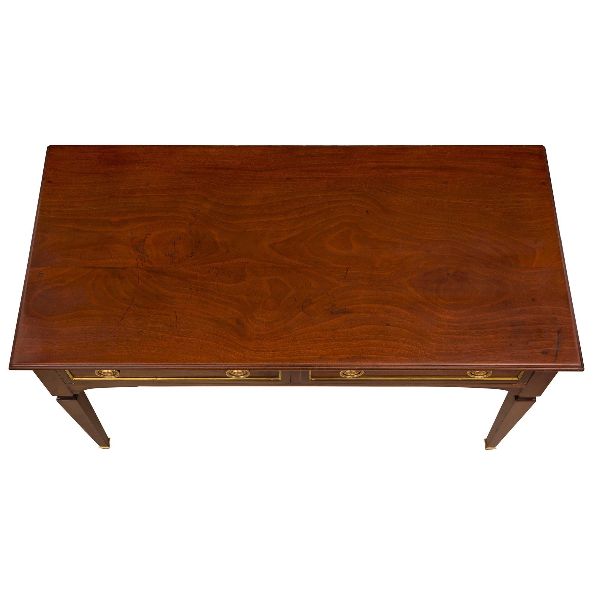 An elegant French 19th century Louis XVI st. Mahogany, brass, and ormolu desk. The desk is raised by fine square tapered legs with elegant mottled fitted ormolu sabots. The straight frieze displays two drawers, each decorated with recessed panels
