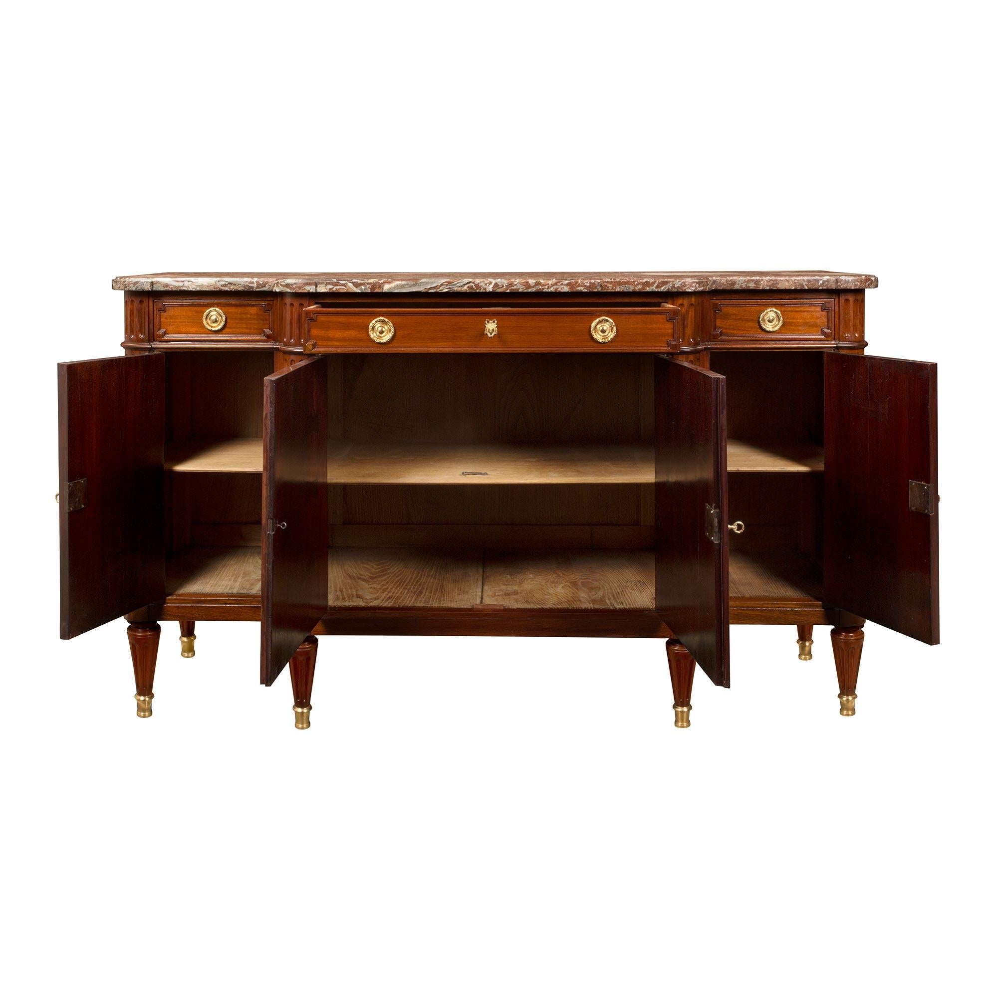 An elegant French 19th century Louis XVI st. mahogany, four door, three drawer buffet. The buffet is raised by beautiful circular tapered legs with fine ormolu sabots. At the center are two doors which display decorative recessed panels and ormolu
