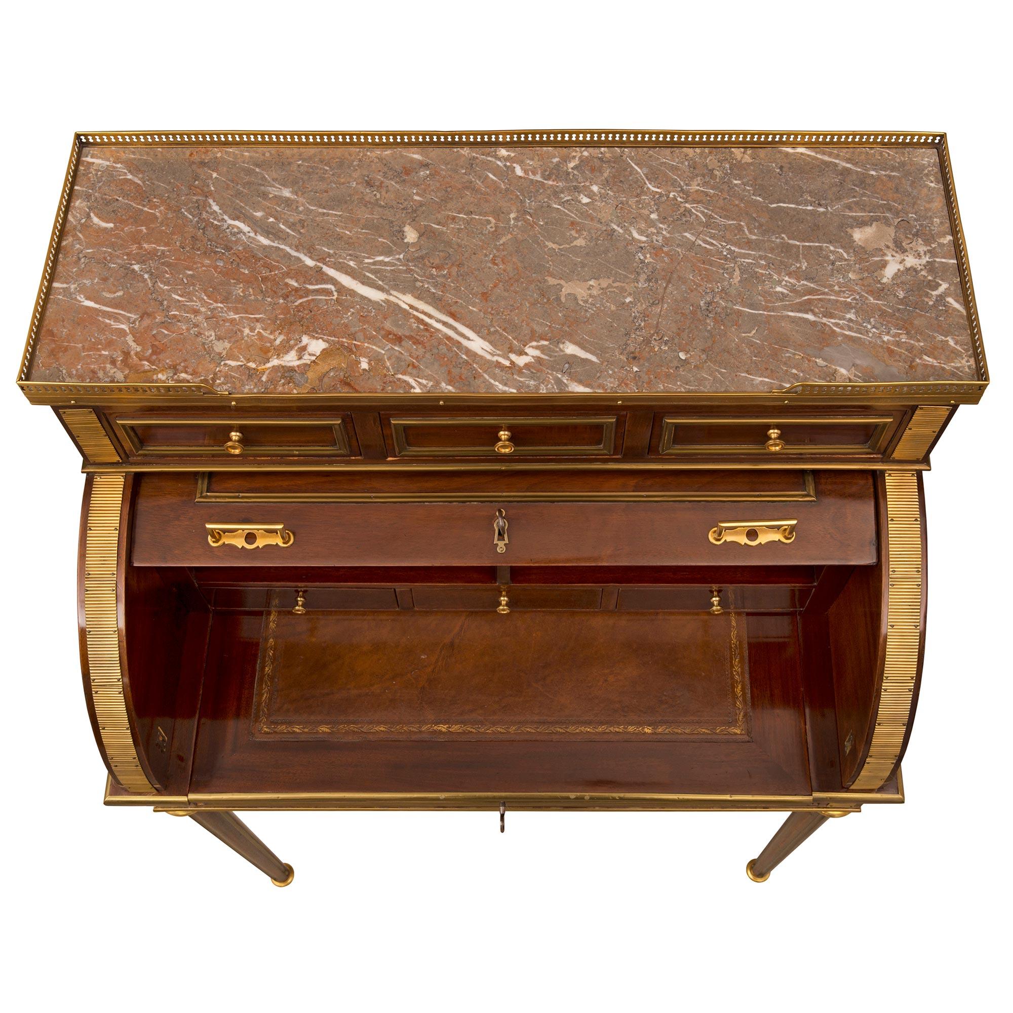 A most elegant French 19th century Louis XVI st. Mahogany, brass, ormolu, and Sarrancolin marble cylinder desk. The desk is raised by slender circular tapered fluted legs with beautiful wonderfully executed fitted brass chandelles, topie shaped