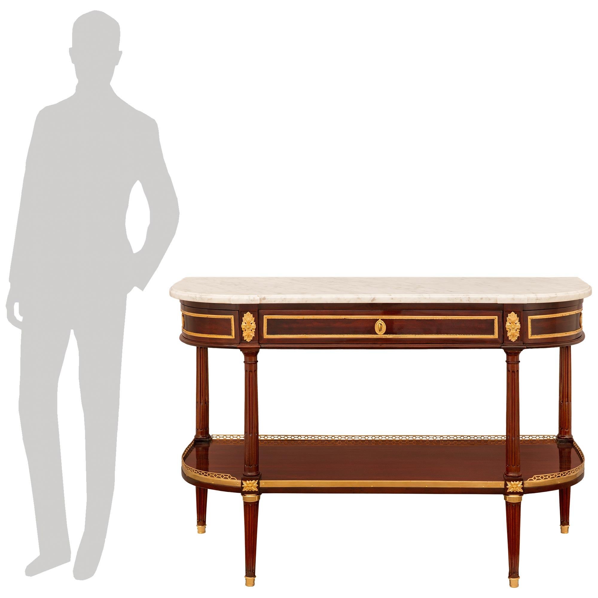 A stunning and high quality French early 19th century Louis XVI st. Mahogany, Ormolu and white Carrara marble console. This wonderful demi lune shaped dessert console is raised on four fluted legs with Ormolu sabots which lead to Ormolu top caps