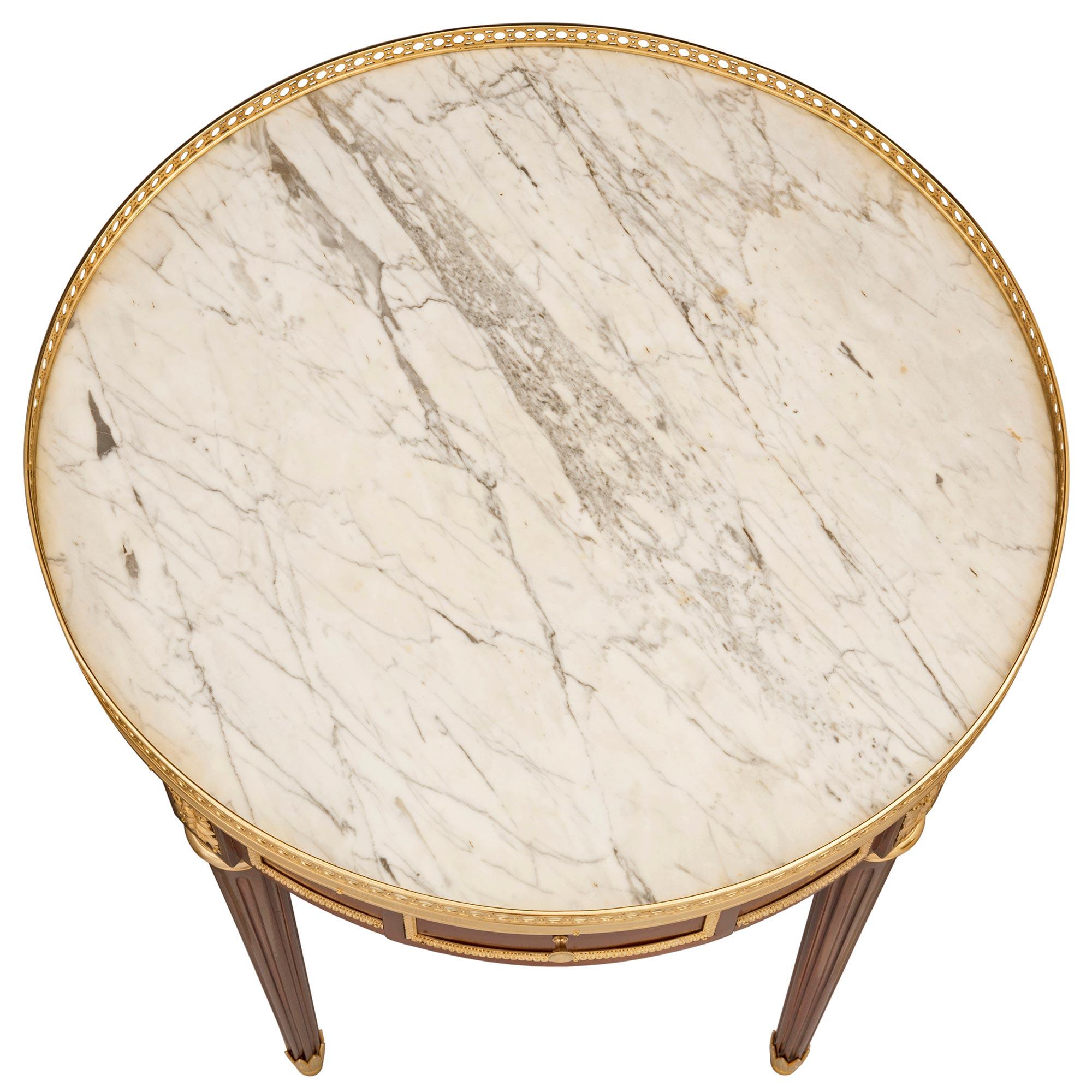 An elegant French 19th century Louis XVI st. mahogany, ormolu, and white Carrara marble side table, attributed to Krieger. The table is raised by fine circular tapered fluted legs with beautifully fitted palmette-designed ormolu sabots and mottled