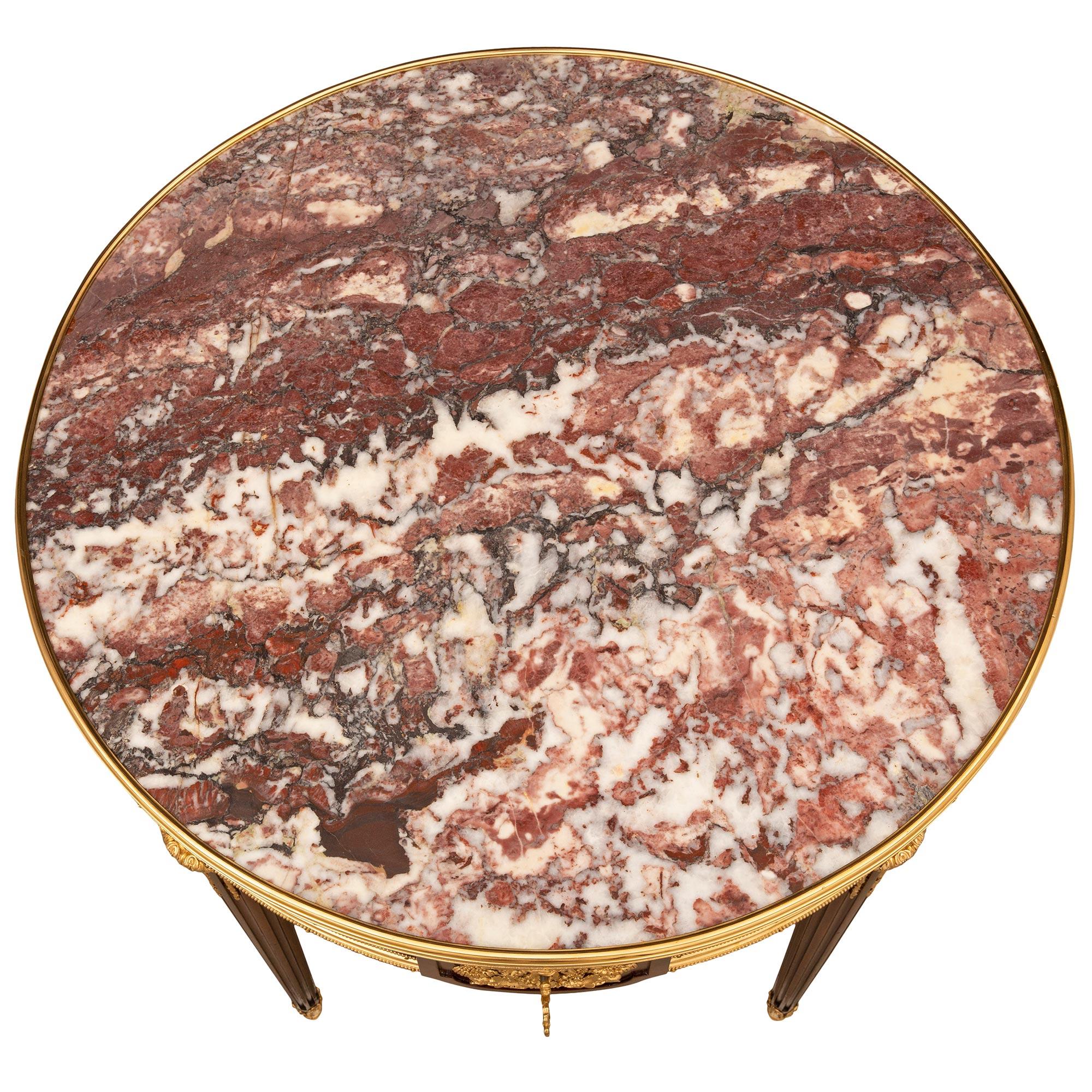 Superbe table d'appoint de très haute qualité, d'époque Louis XVI et Belle Époque, en acajou, bronze doré et marbre Escalette, attribuée à la Maison Krieger. La table est surélevée par d'élégants pieds circulaires fuselés et cannelés, avec des