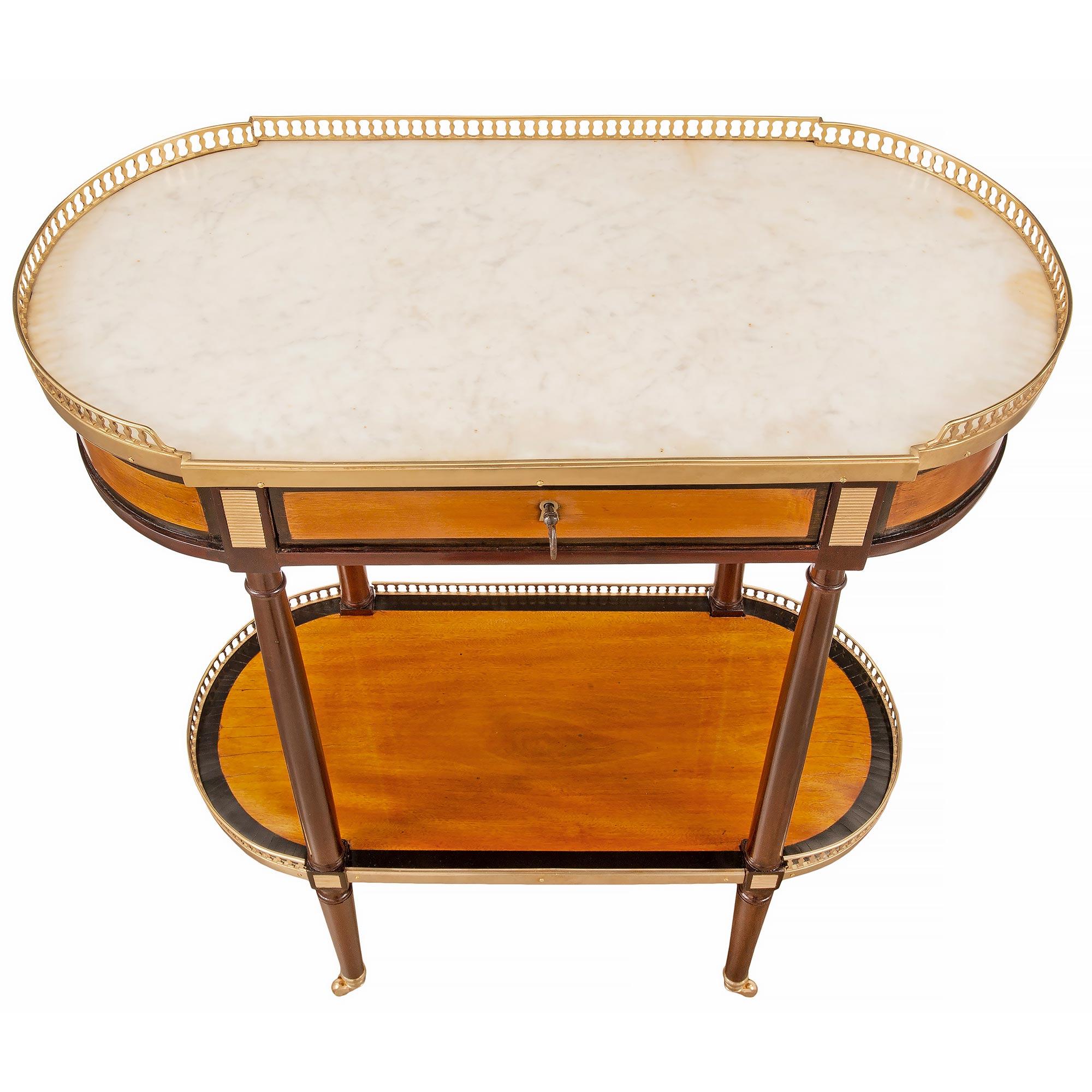 Très élégante table d'appoint ovale de style Louis XVI en acajou, bois de satin et bronze doré. La table est surélevée par de fins pieds circulaires coniques avec leurs roulettes originales en bronze doré. Les pieds sont reliés par un étage de