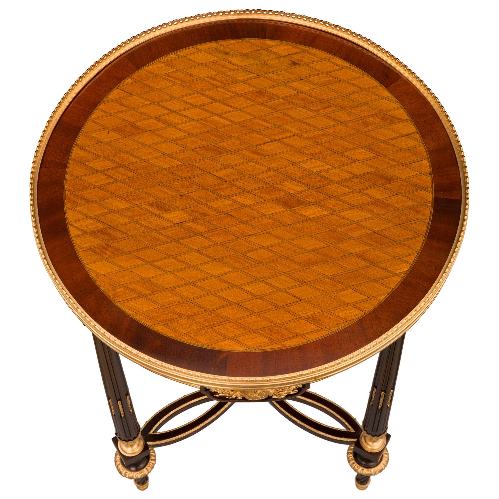 An elegant French 19th century Louis XVI st. mahogany, tulipwood, charmwood, and ormolu side table. The circular table is raised by beautiful circular tapered feet with a most decorative fluted spiral design, topie shaped ormolu sabots, and foliate