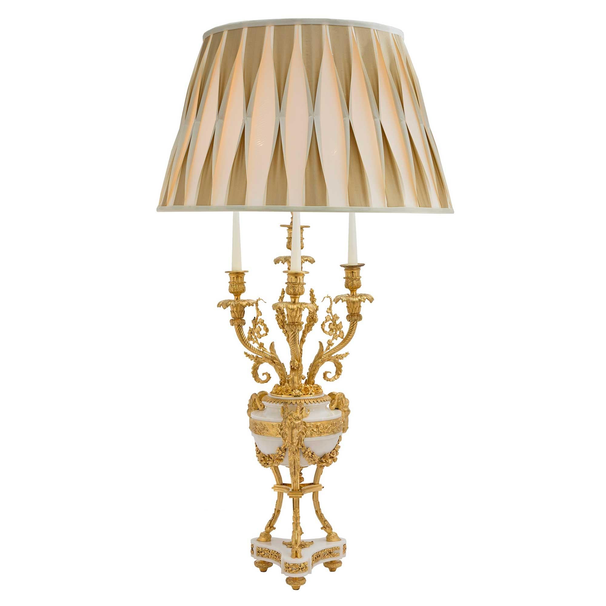 Une paire de magnifiques lampes candélabres françaises du 19ème siècle de style Louis XVI en marbre blanc de Carrare et bronze doré. Chaque lampe repose sur des pieds en topie en bronze doré, sous une base triangulaire en marbre avec des montures en