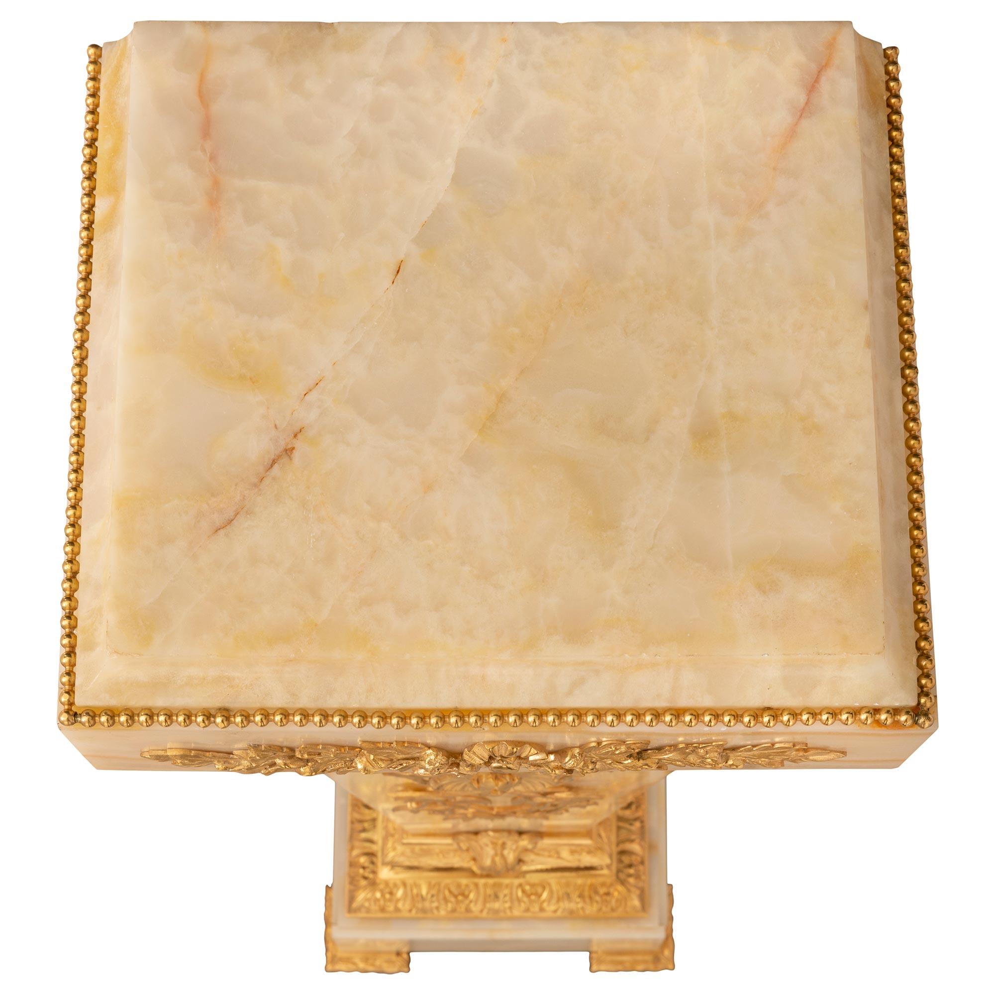 Colonne à piédestal en onyx et bronze doré, de style Louis XVI, datant du XIXe siècle. Le piédestal est surélevé par une base carrée avec des pieds en laurier fleuri et un impressionnant support en bronze ciselé et feuillagé avec une bande de
