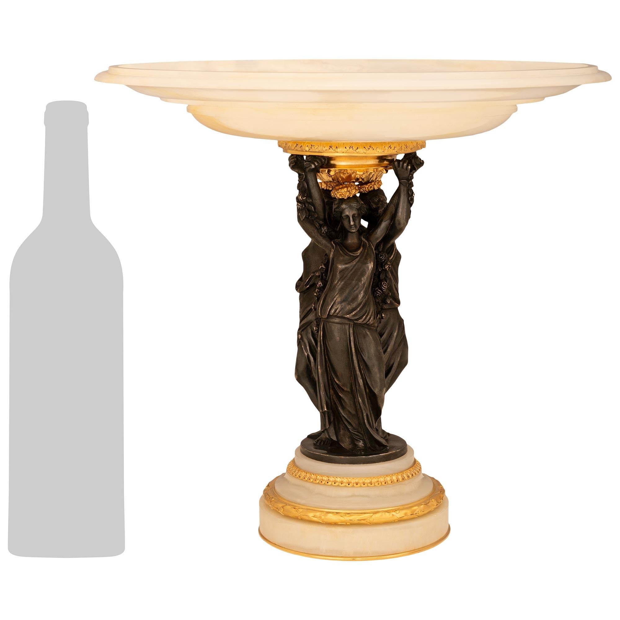 Un elegante e pregiato centrotavola francese del XIX secolo in stile French Belle Epoque con onice, ormolu e bronzo patinato. Questo meraviglioso centrotavola è sollevato da una base a tre livelli con una fascia inferiore a quarto di giro in Ormolu.
