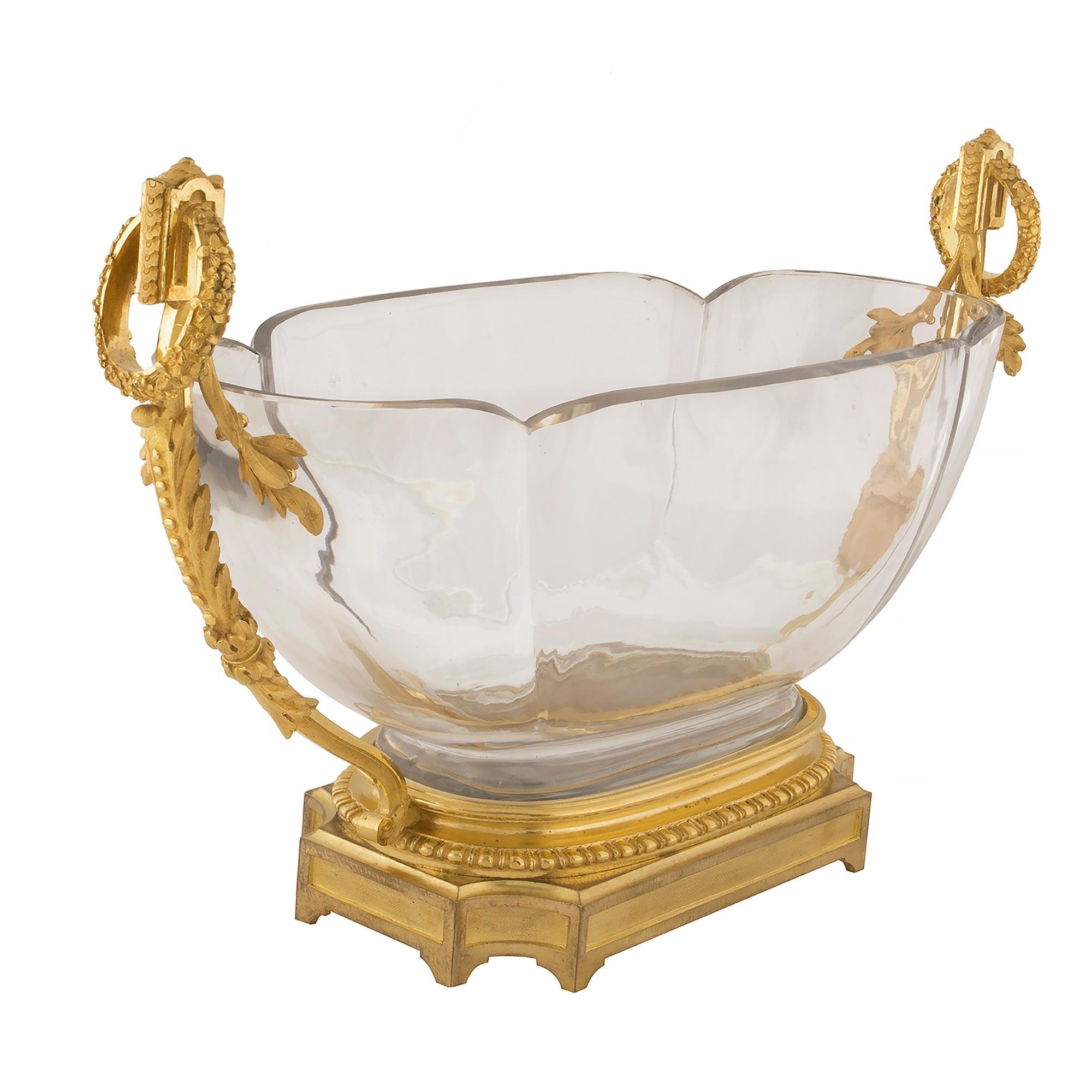An elegant French 19th century Louis XVI St. ormolu and Baccarat crystal centerpiece bowl. The centerpiece is raised by a rectangular ormolu base with concave corners and decorative recessed panels. The bowl is supported by a fine mottled base with