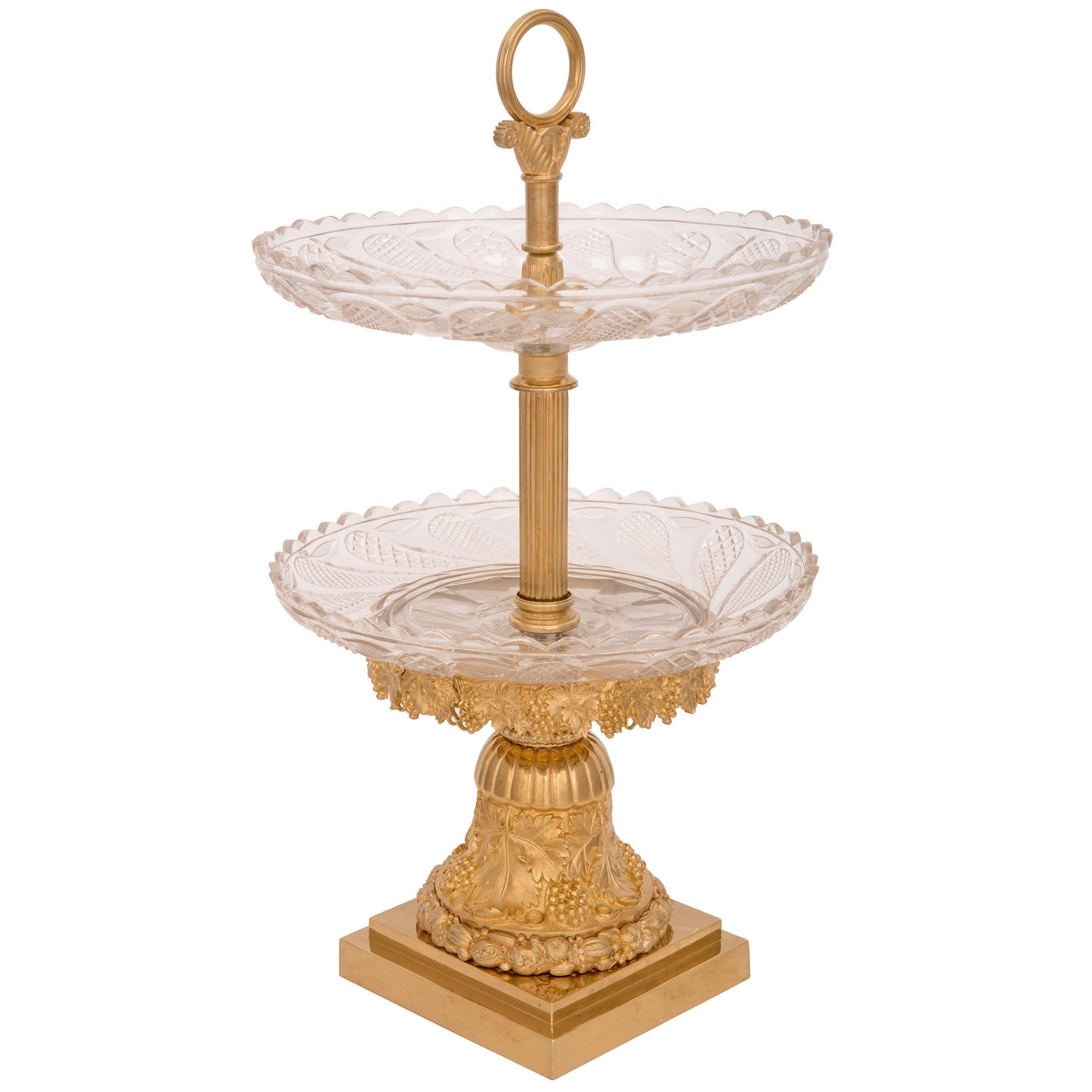 An exquisite French 19th century Louis XVI st. ormolu and Baccarat crystal two tiered presentoir centerpiece. The presentoir is raised by a square base with an elegant stepped design and a stunning wrap around band with a most unique richly chased