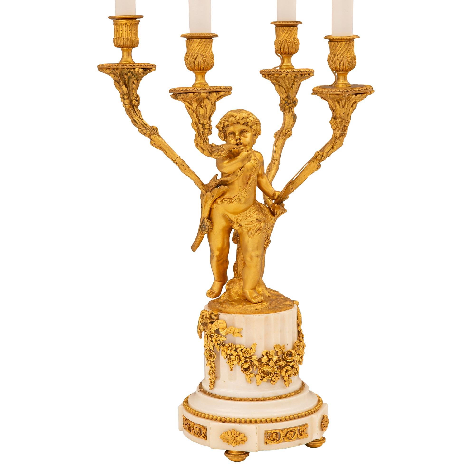 Une charmante et extrêmement élégante lampe candélabre française du 19ème siècle de style Louis XVI en bronze doré et marbre blanc de Carrare. La lampe à quatre bras est surélevée par de fins pieds en bronze doré sous une base circulaire cannelée en