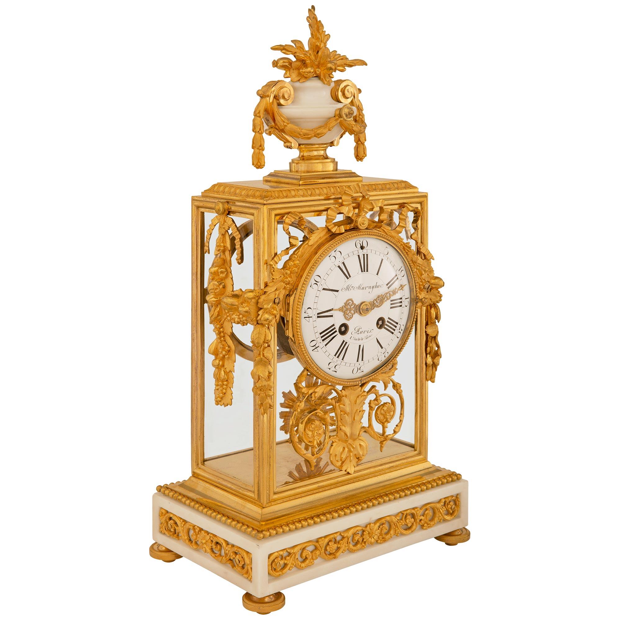 A stunning and high quality French 19th century Louis XVI st. Ormolu and white Carrara marble clock, signed Maison Marnyhac. This exquisite mantel clock is raised by a rectangular white Carrara marble base with four recessed panels containing Ormolu