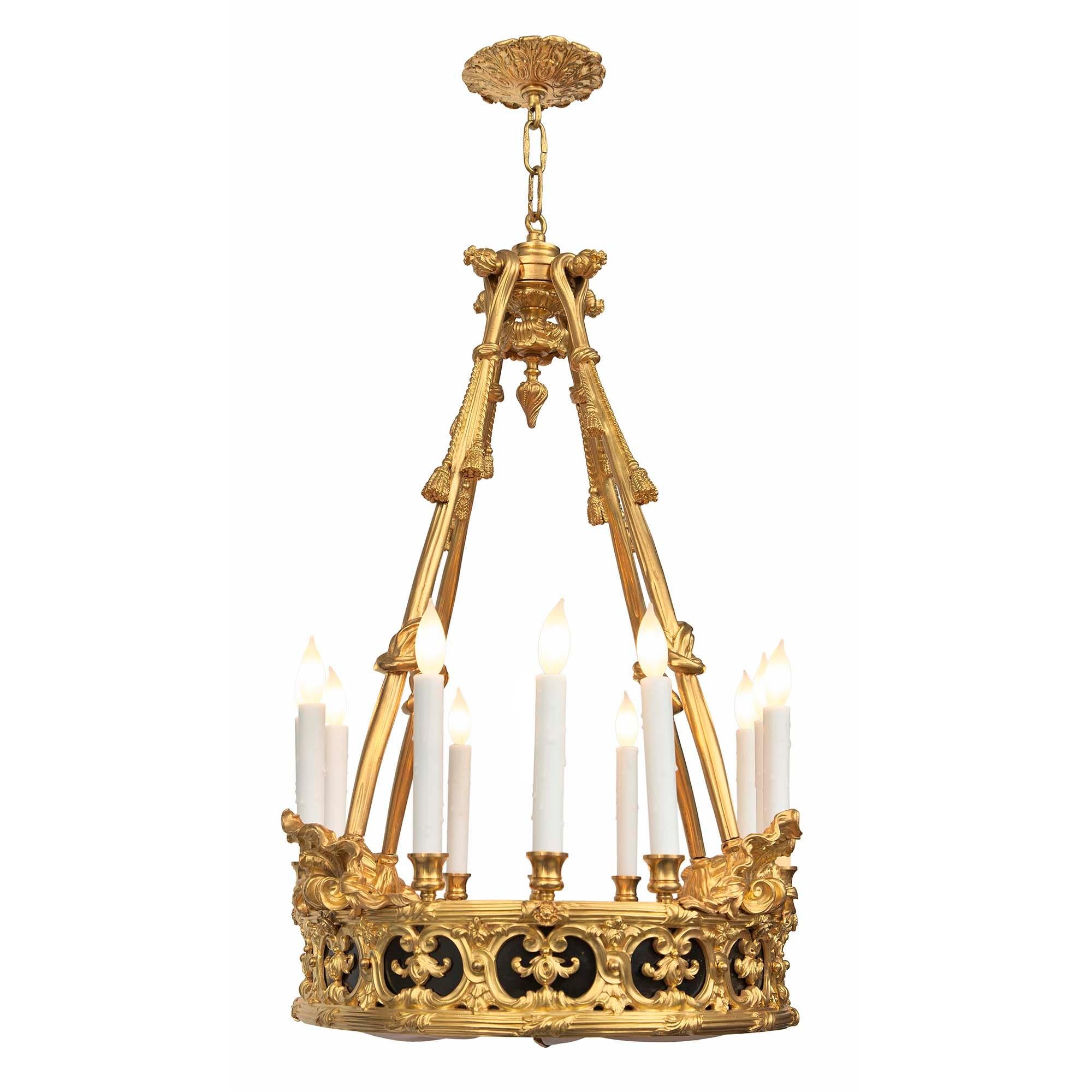 A spectacular French 19th century Louis XVI st. ormolu and patinated bronze chandelier. The twelve arm chandelier is centered by a striking bottom ormolu finial with a pierced foliate design and elongated foliate movement gathering the silk