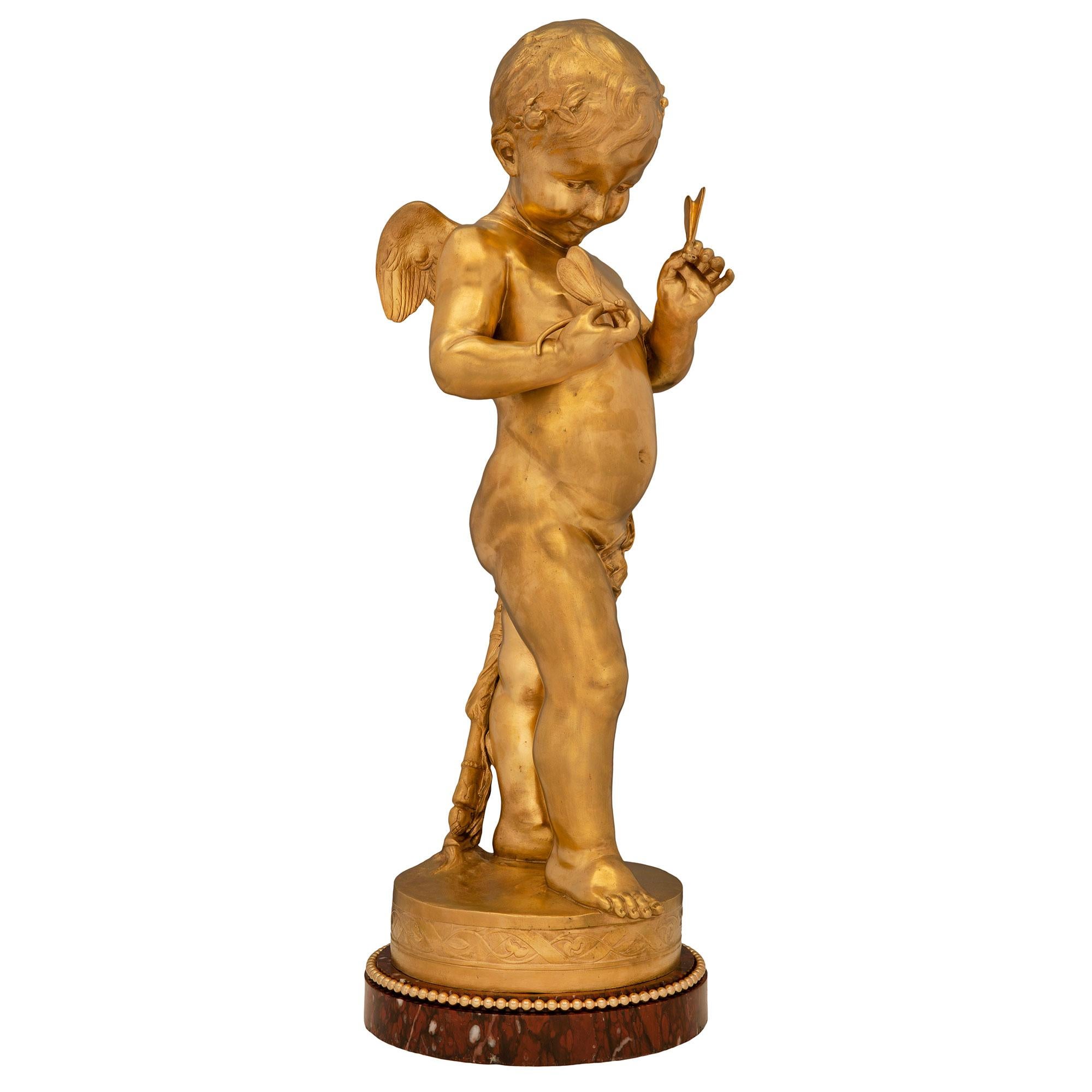 Statuette de grande qualité et extrêmement charmante en marbre Rouge Griotte et bronze doré de style Louis XVI du 19ème siècle. La statue est surélevée par une élégante base circulaire en marbre Rouge Griotte avec une fine bande perlée en bronze