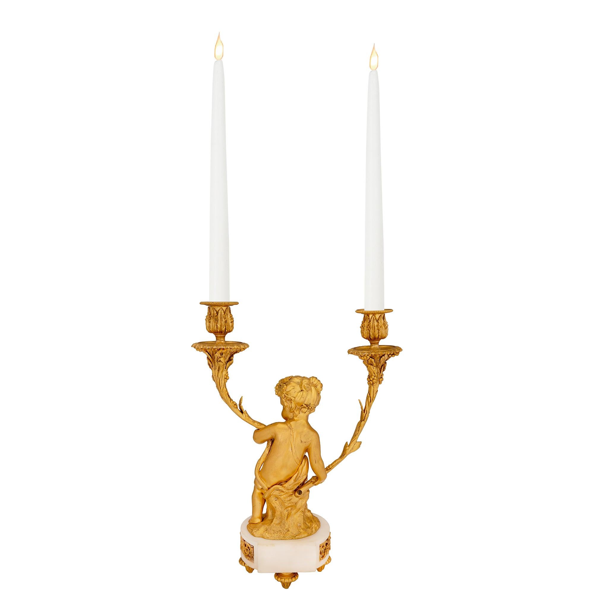 Un exquis candélabre français du 19ème siècle de style Louis XVI en bronze doré et marbre blanc de Carrare, modelé d'après Clodion. Le candélabre à deux bras est surélevé par de fins pieds en forme de topie sous la base en marbre blanc de Carrare